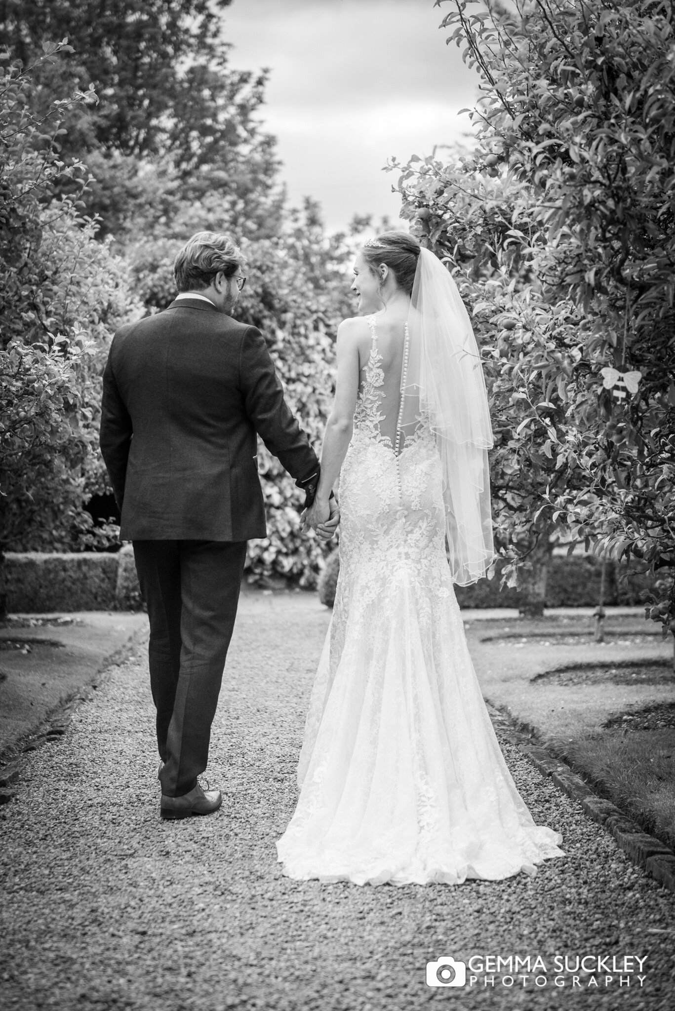 black and white photo of the bride and groom walking down a garden path at east riddlesden hall 