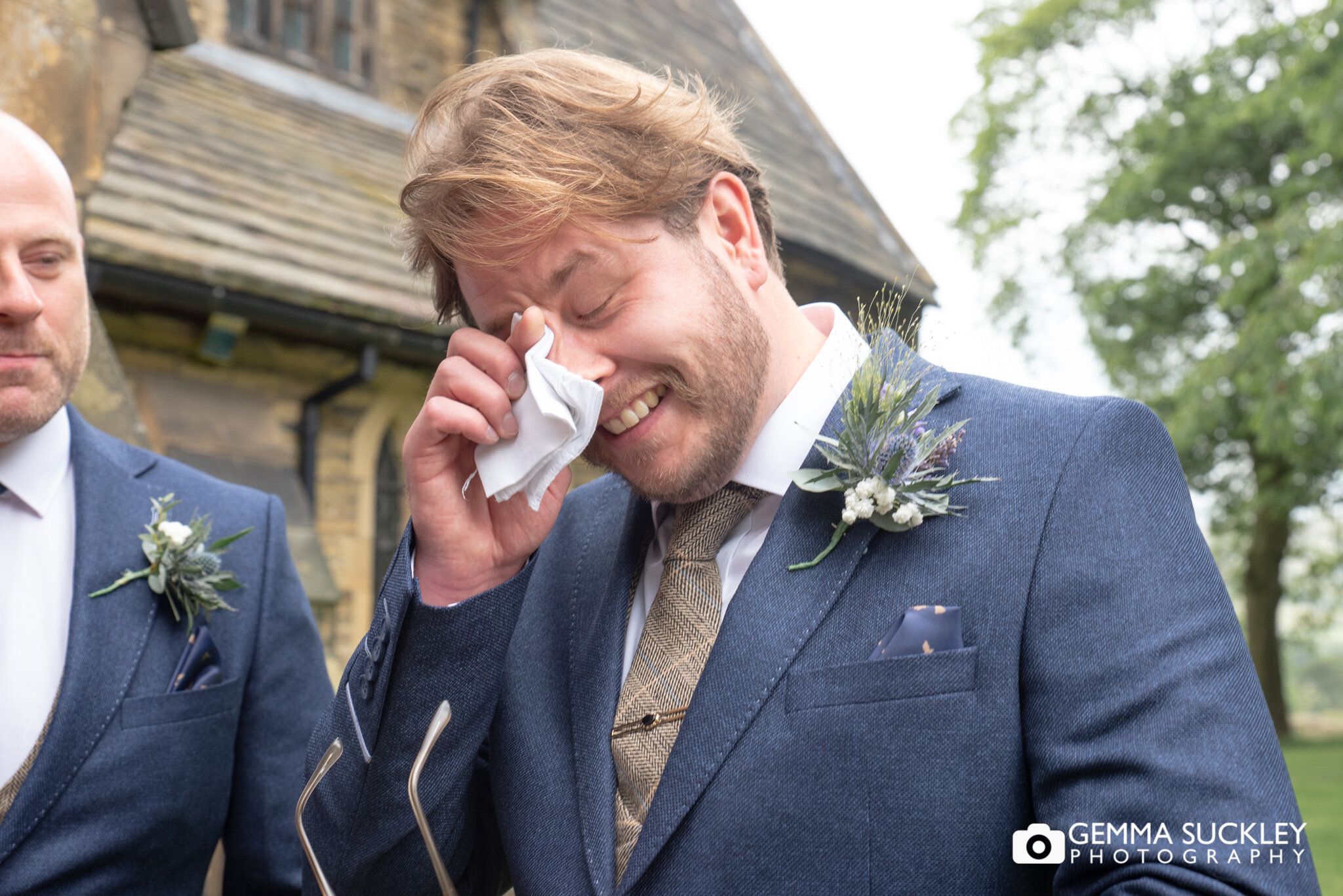 the groom wiping his eyes with a tissue outside the church