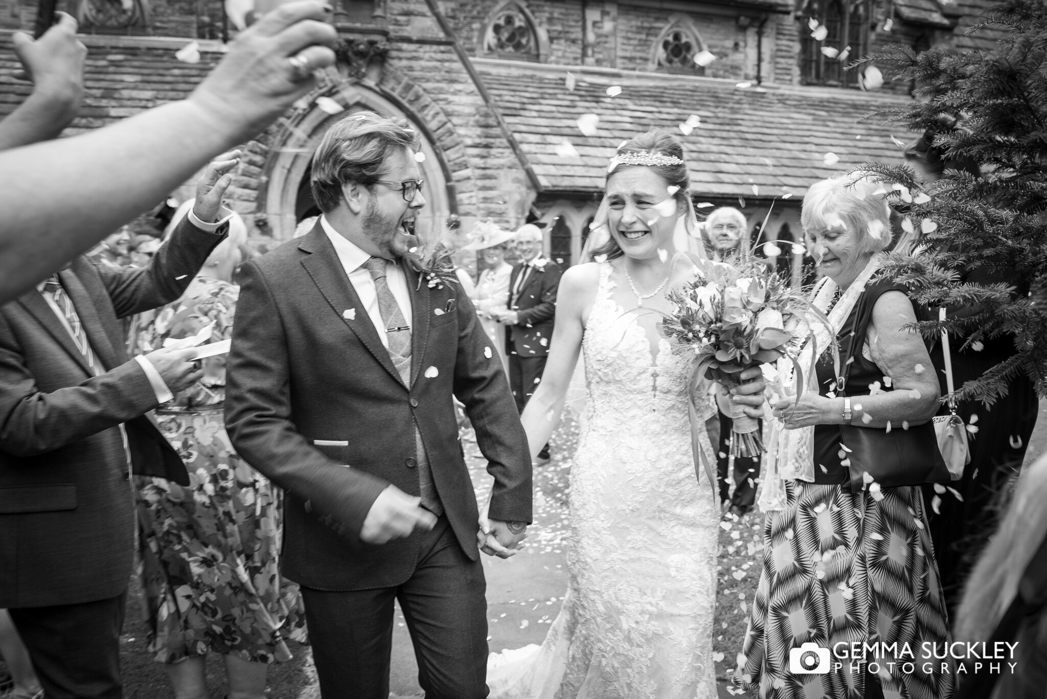 bride and groom laughing as the guests throw confetti at them 