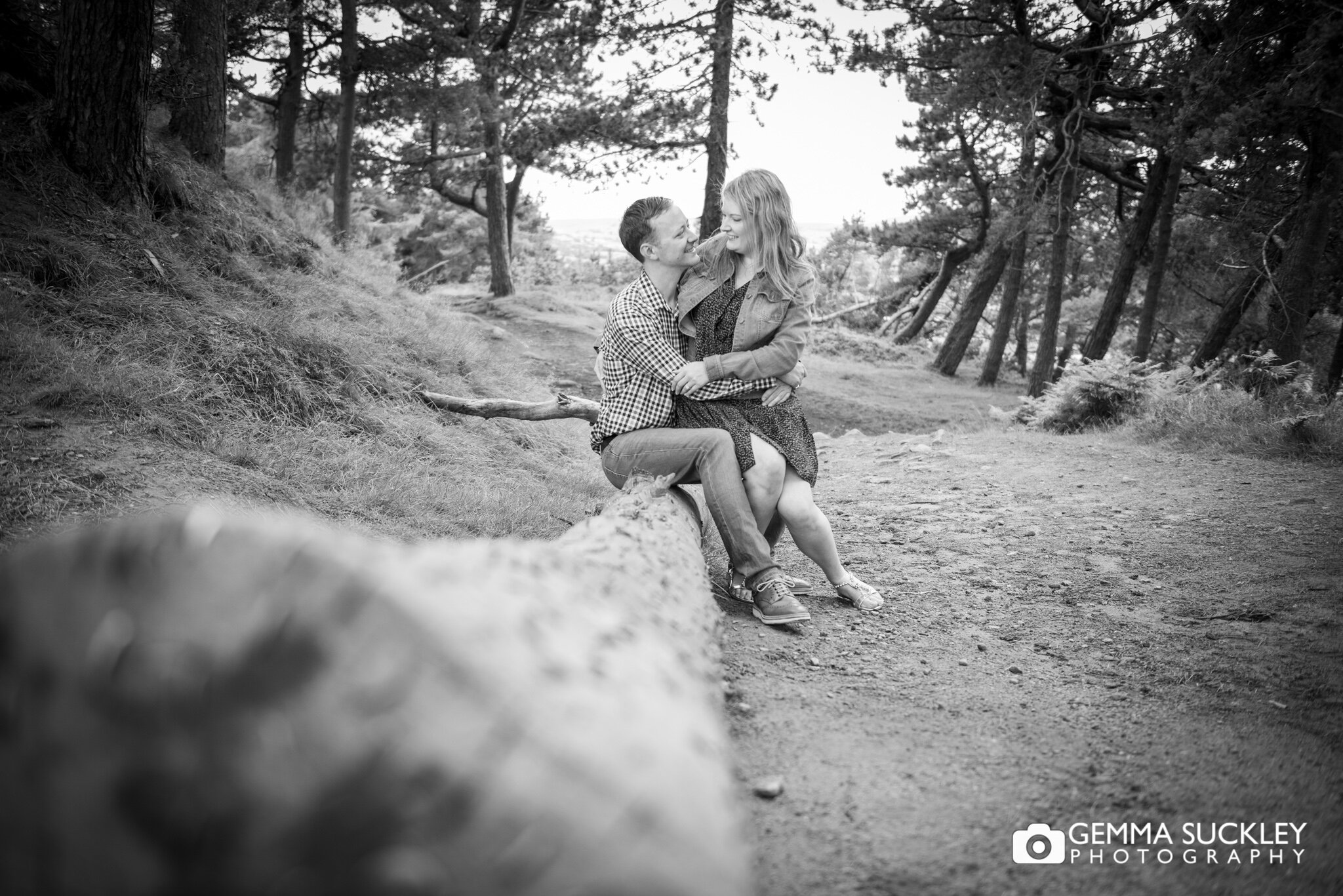 black and white photo of a couple sat on a fallen branch