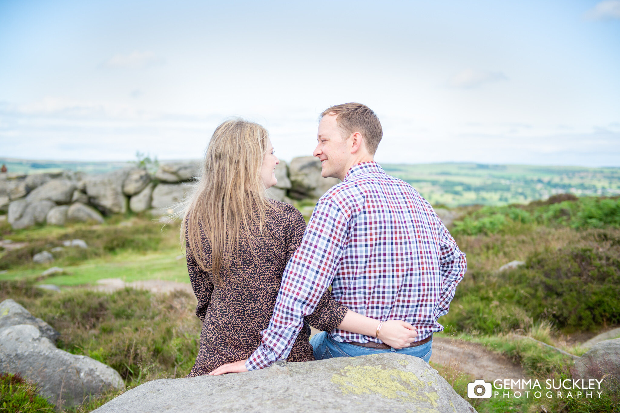 a couple sitting on a rock on ilkely moor for their pre-wedding photos
