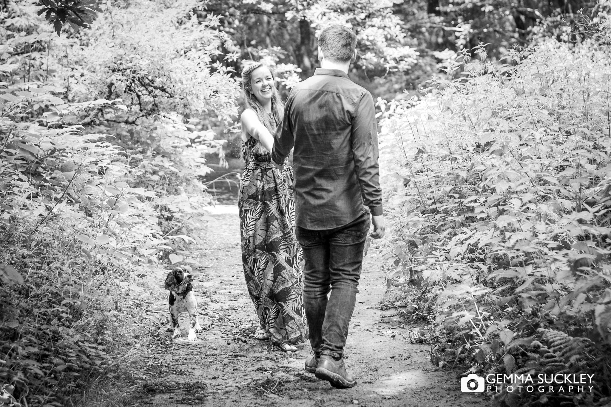an enageged couple walking in the wood with their puppy