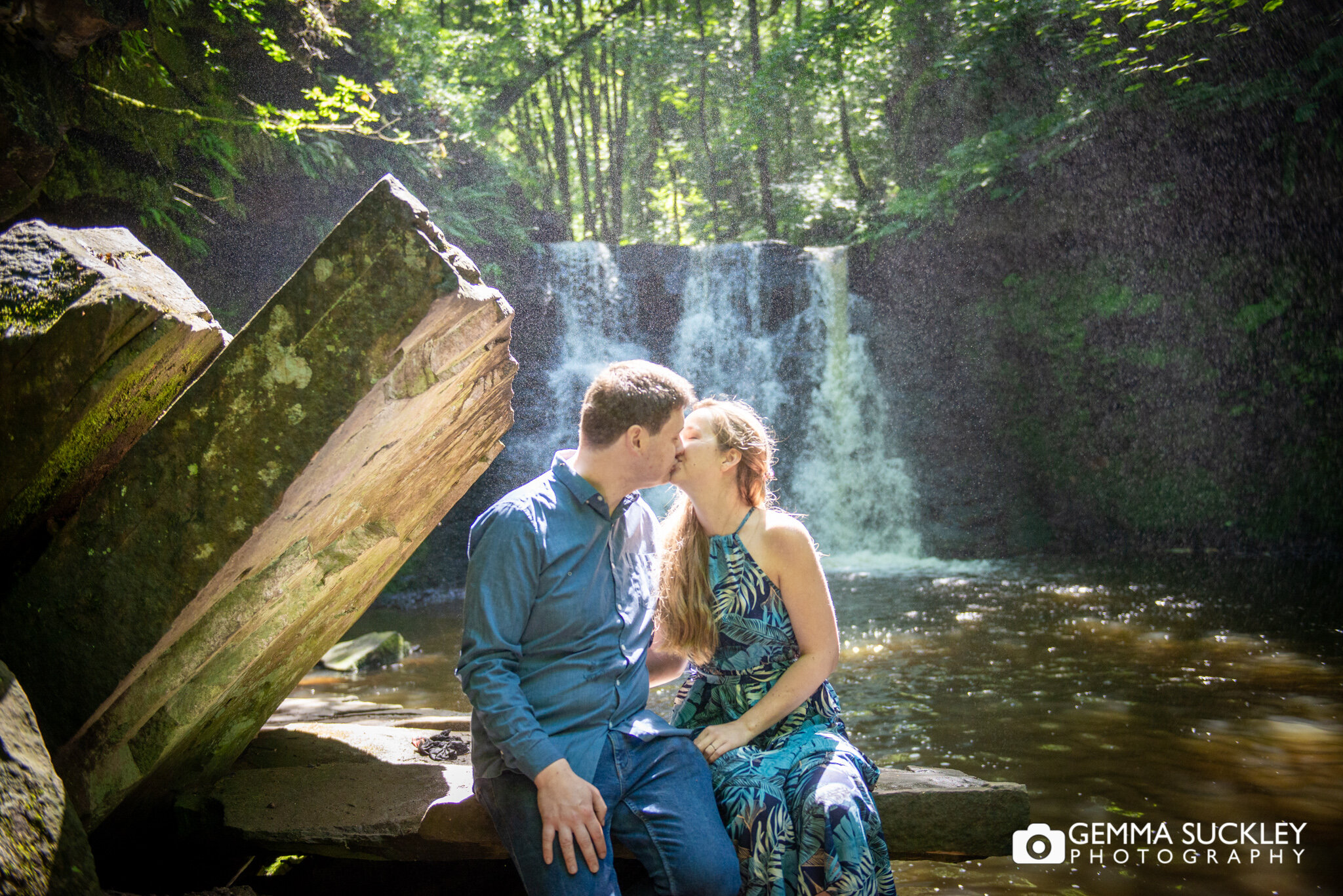 a couple kissing in front of a waterfall for their engagement photo