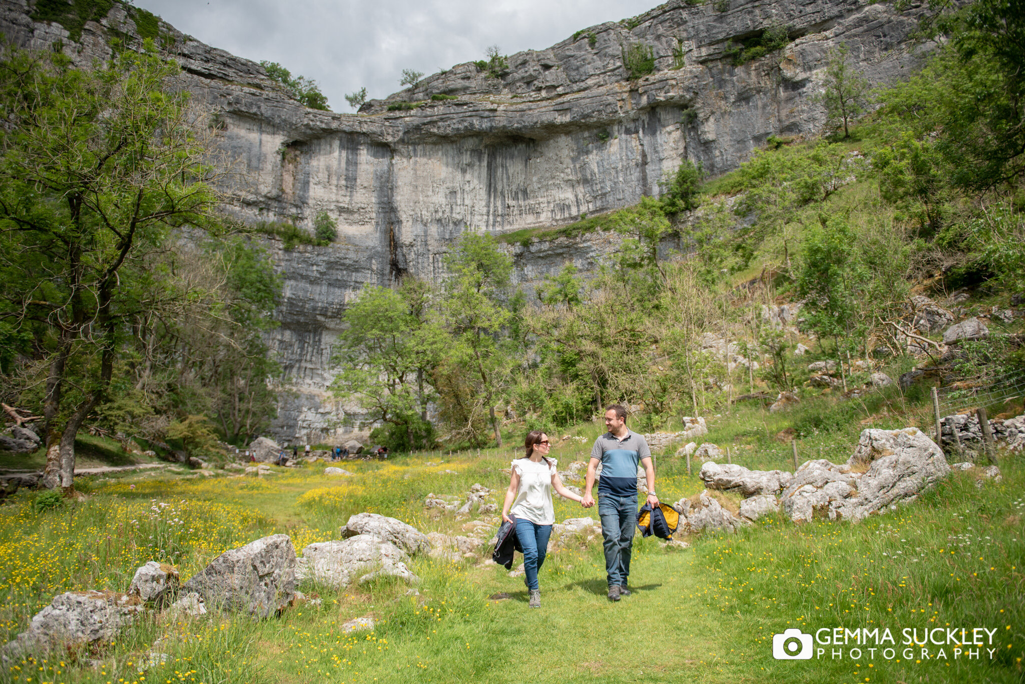 a couple walking towards the camera with malham cove in the background