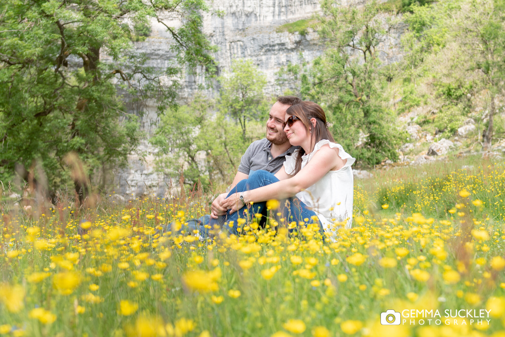an engaged couple sitting in the buttercups in malham for their engaged photo shoot