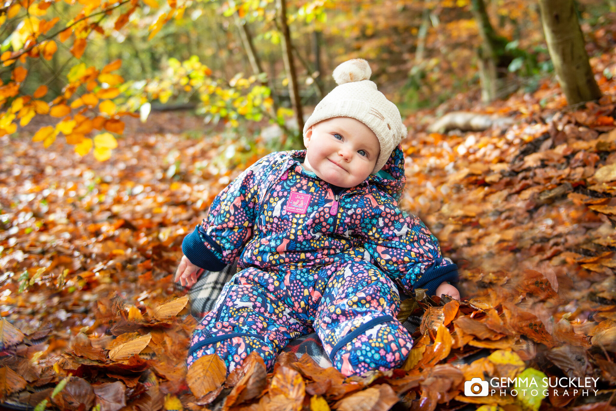 a baby sitting on a pile of autumn leafs in skipton wood