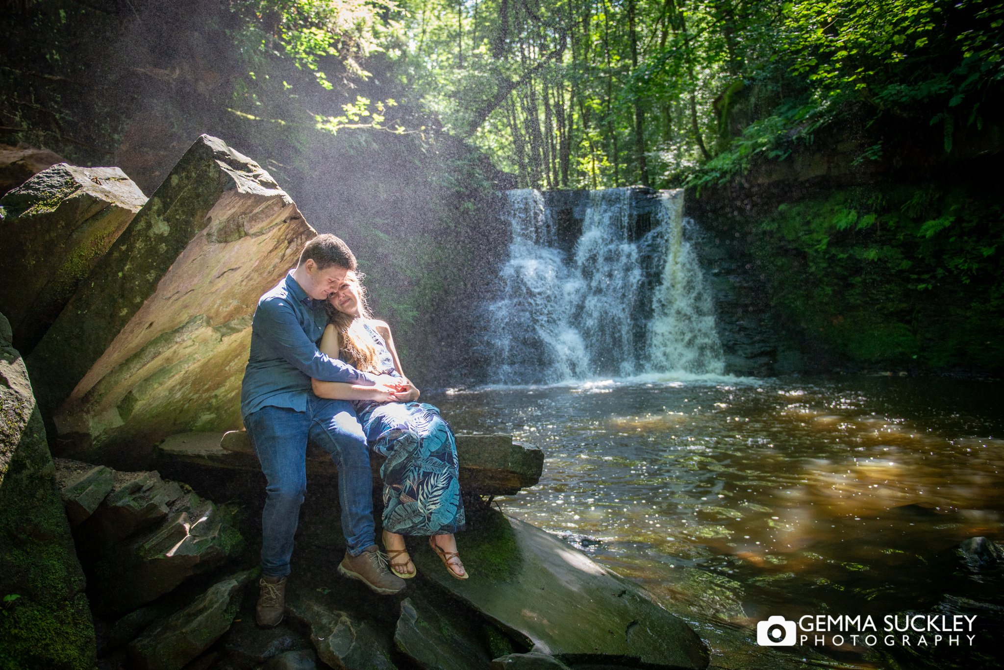 an engagement photo of a cople sittin gon a rock with a beautiful waterfall behind them in cullingworth