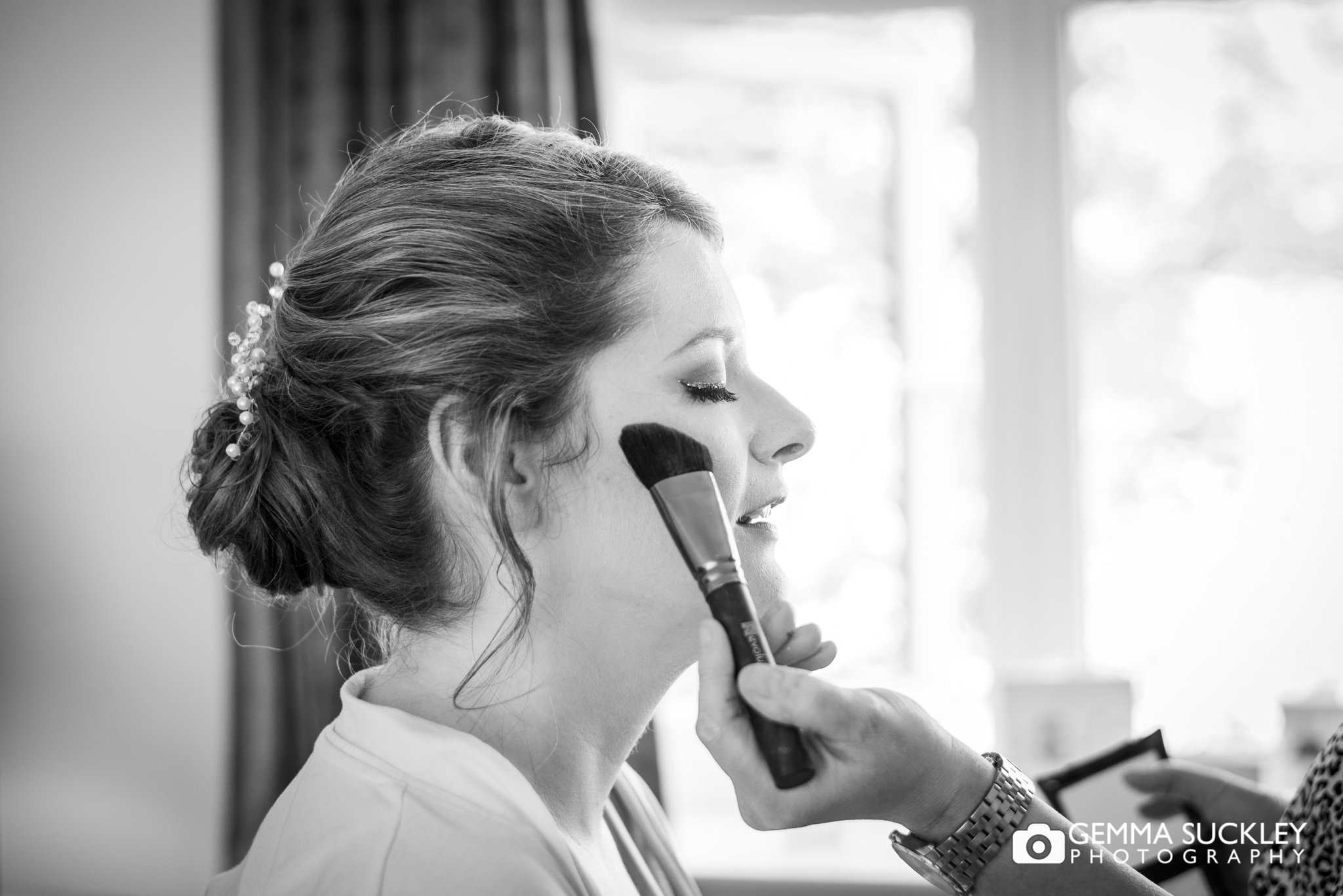 black and white wedding photography of makeup being applied to the bride