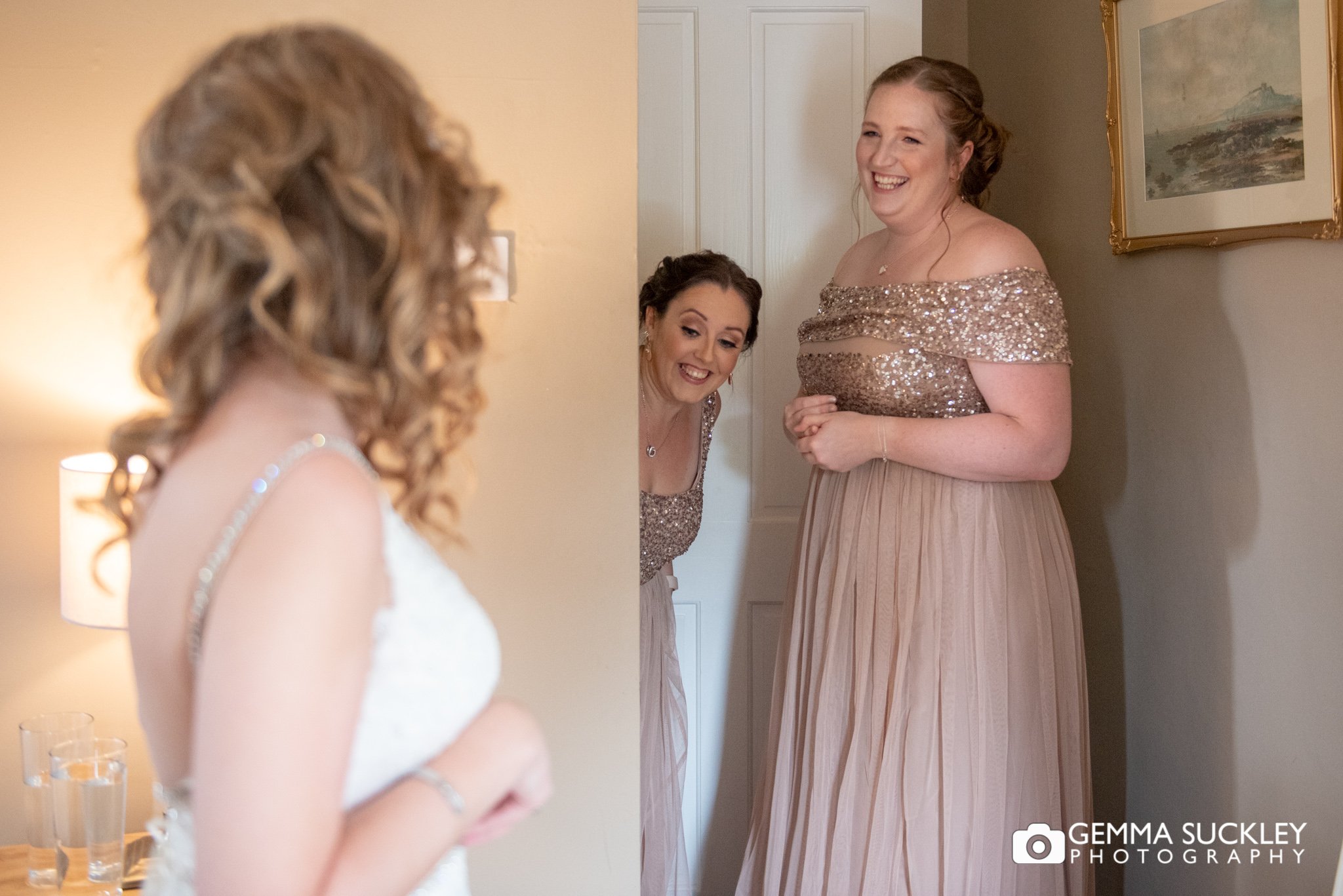 two bridesmaids peeking at the bride in her dress