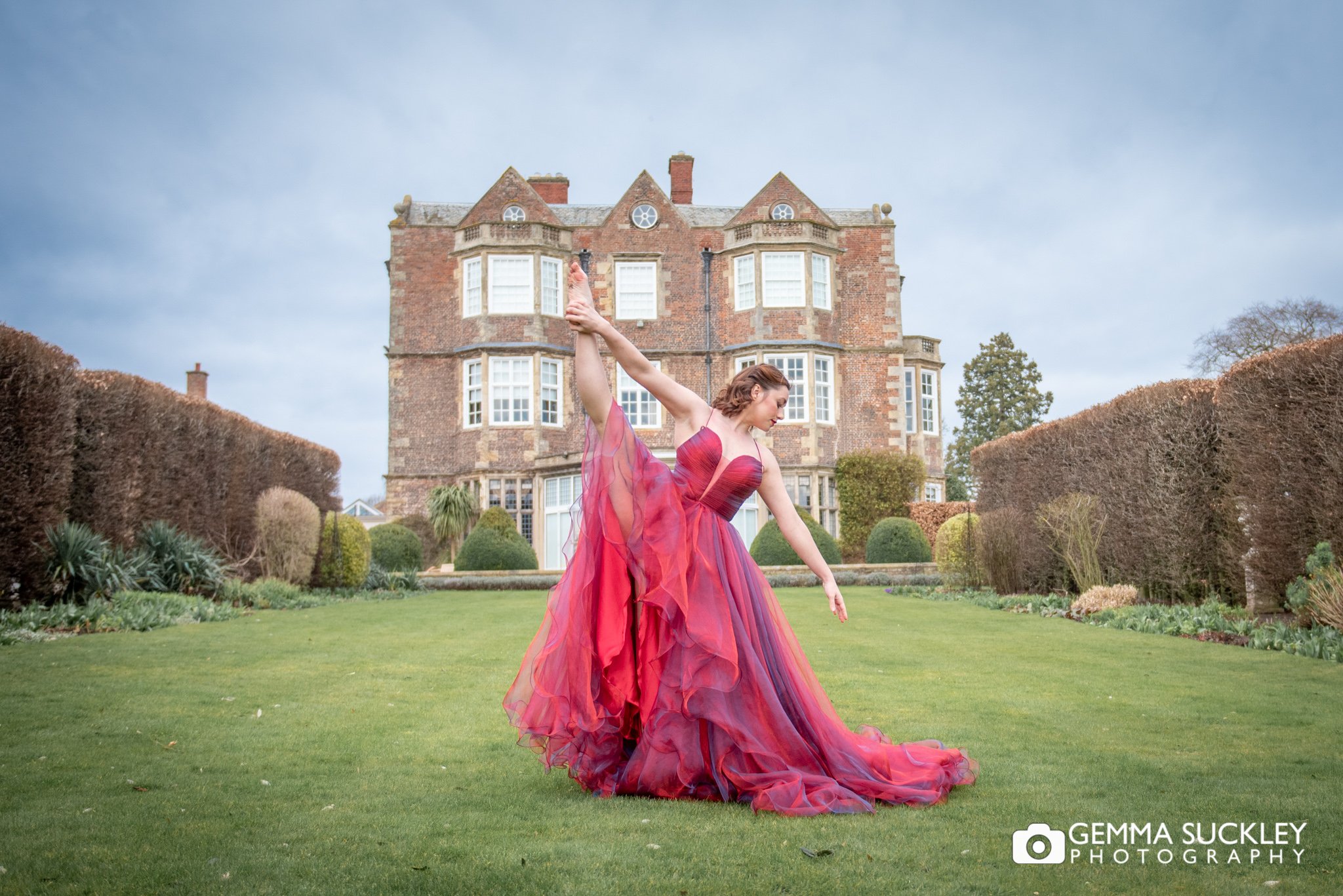 a ballet dancer in a red dress in front of goldborough hall 