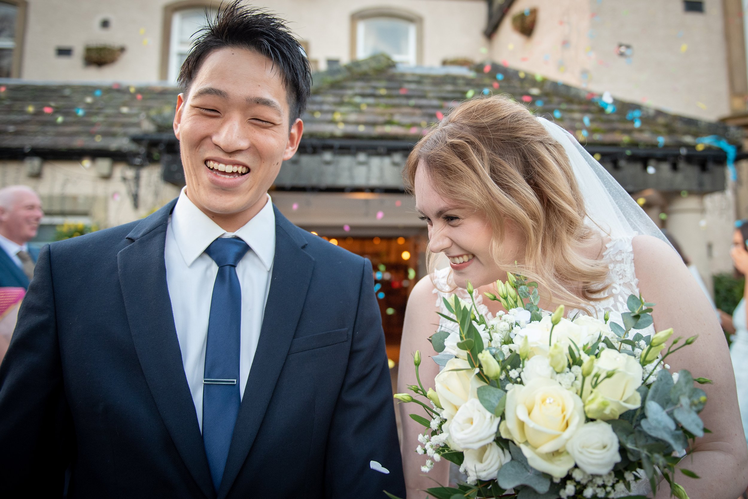 A bride and groom laughing outside steeton hall as confetti is thrown at them