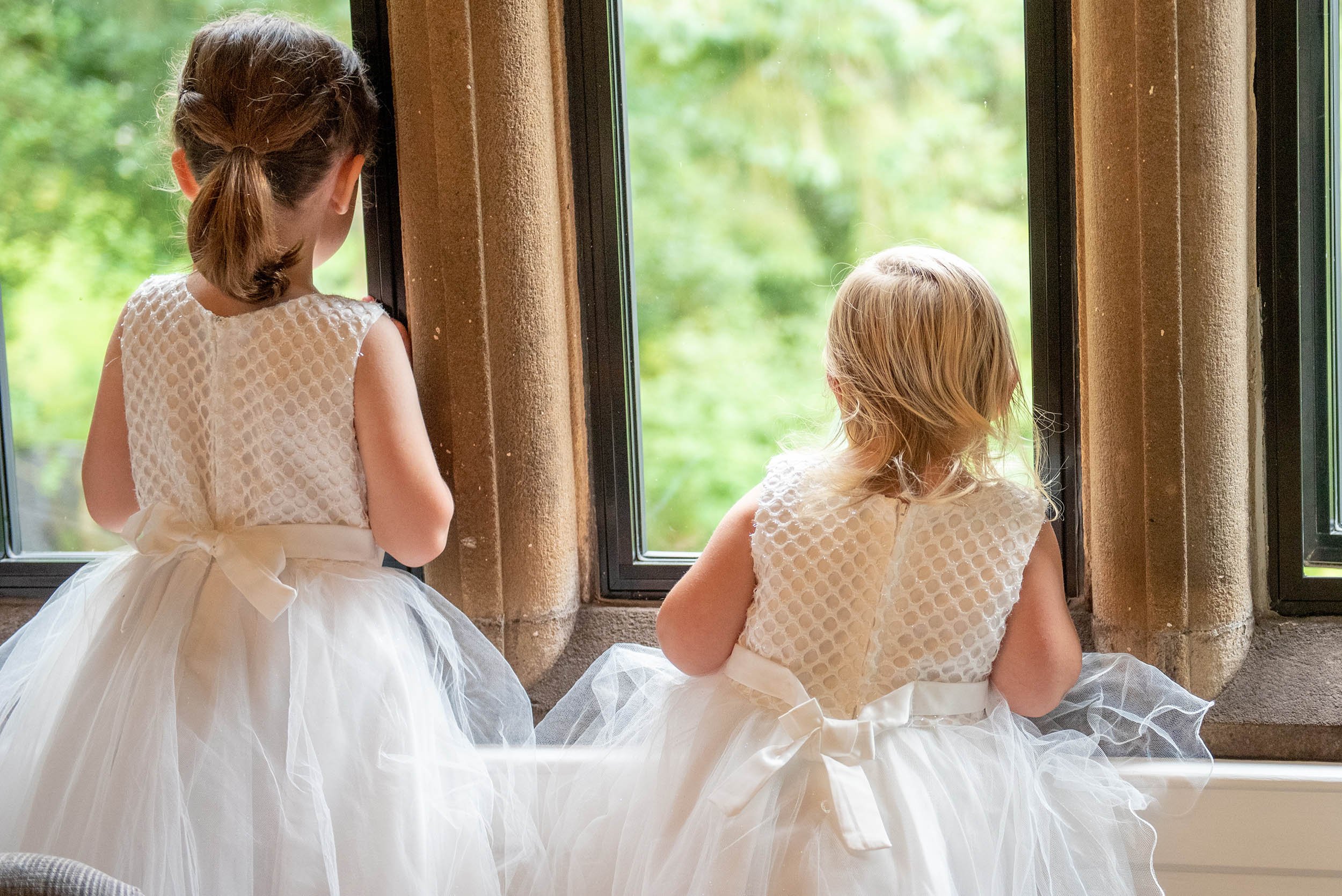 two flower girls looking out the windown at outershaw hall during bridal preparation