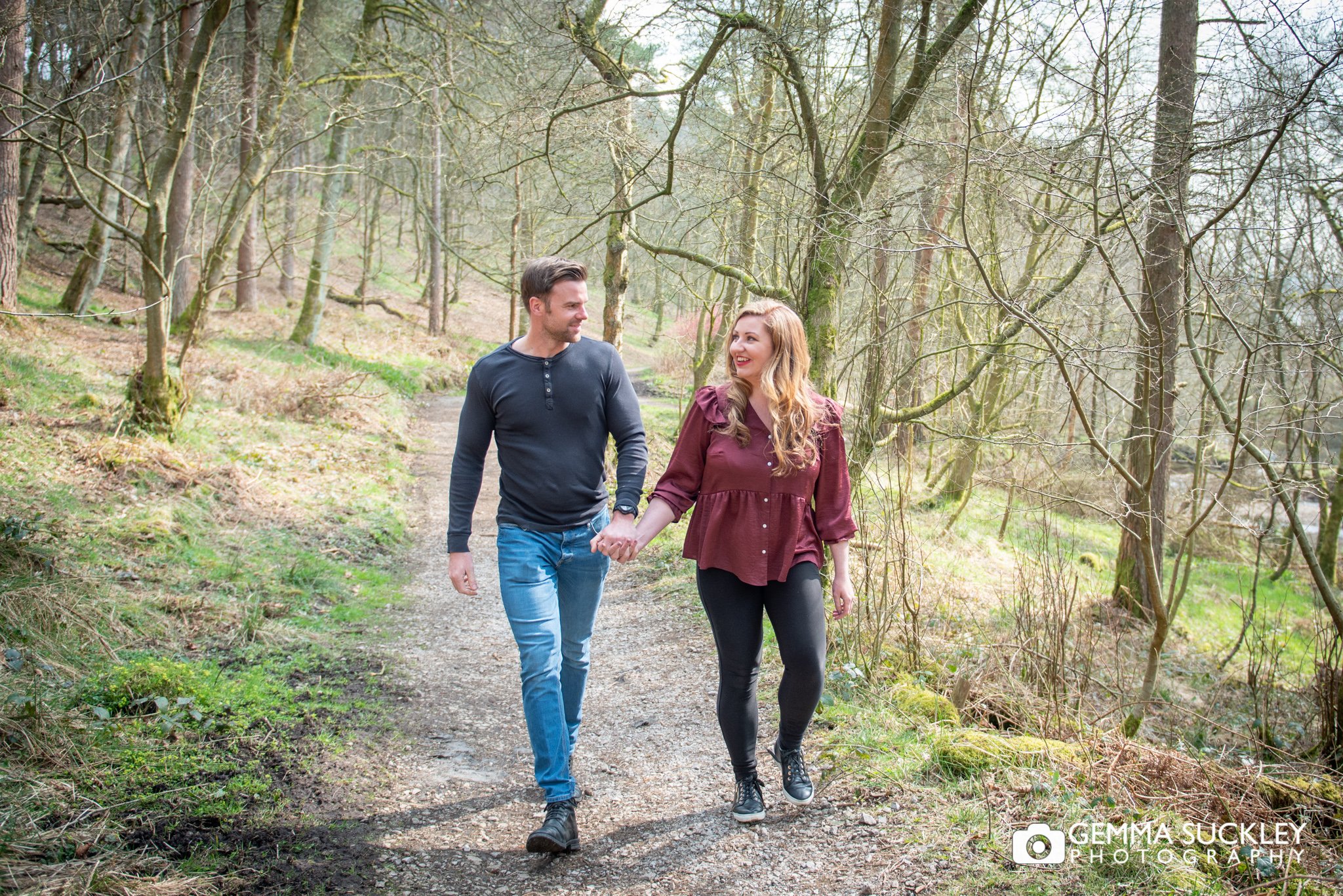 an engaged couple walking through the woods at ogden water country park
