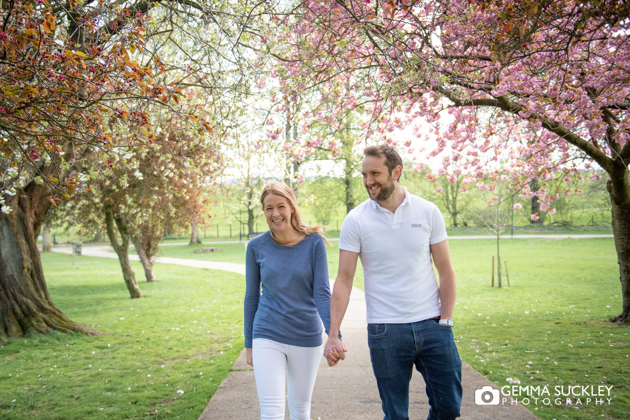 an engaged couple walk under the blossom trees in skipton park