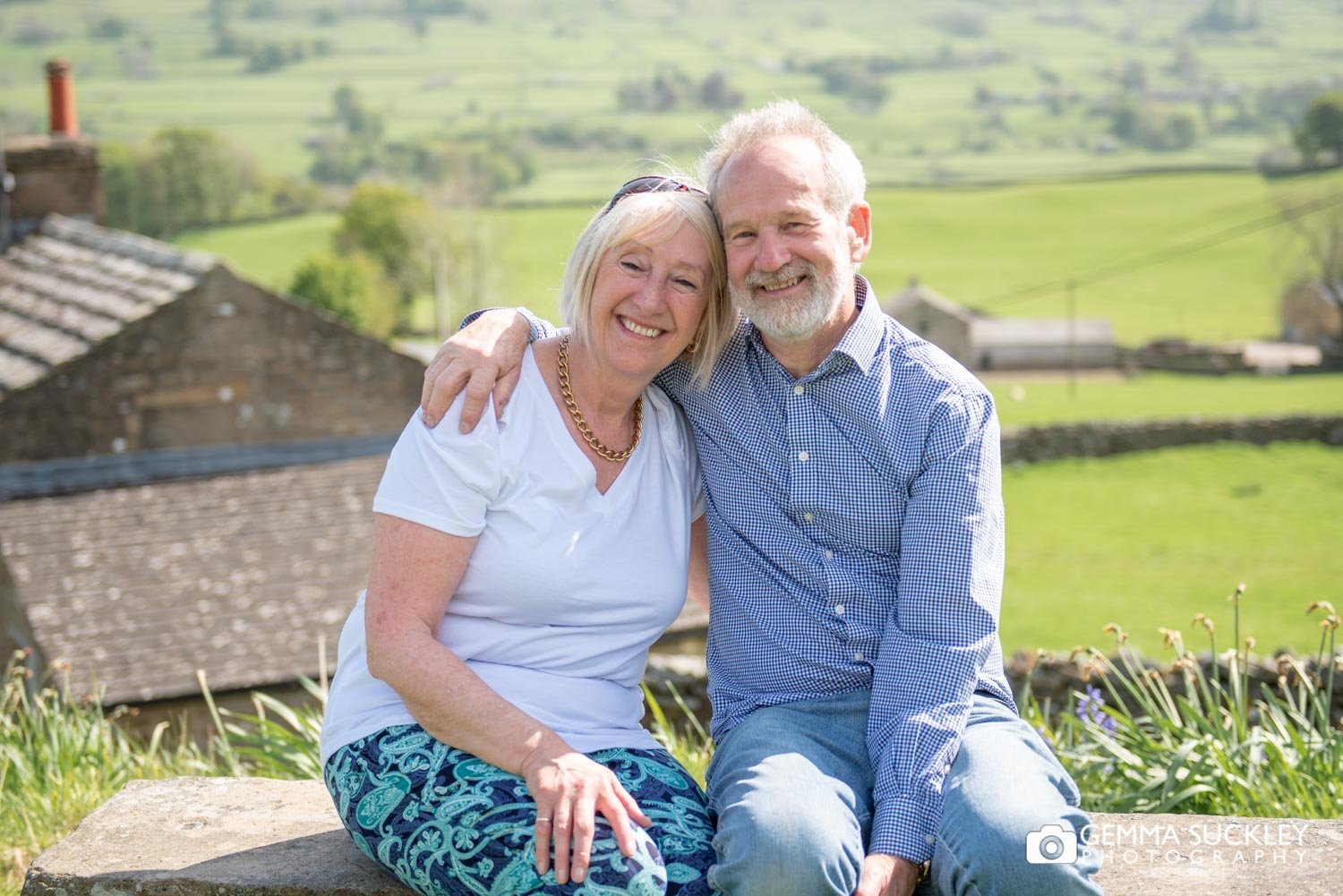 a couple  smiling with the views of hawes behind them 