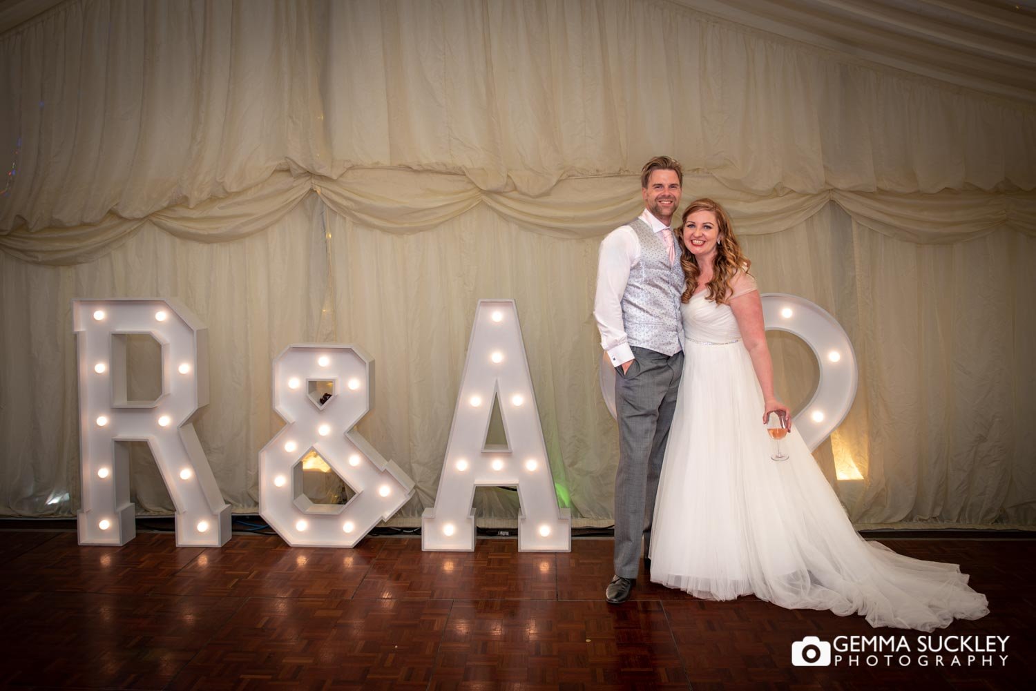 bride and groom stood in front of light of wedding letters