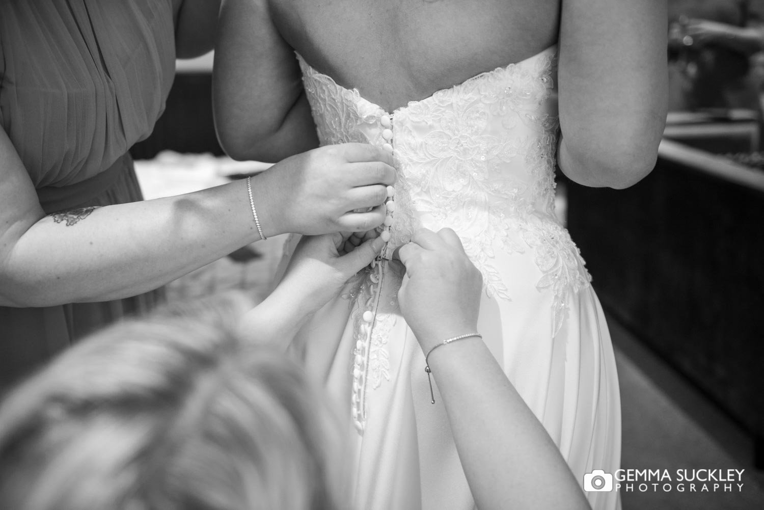 bridesmaid doing up buttons on the brides wedding dress