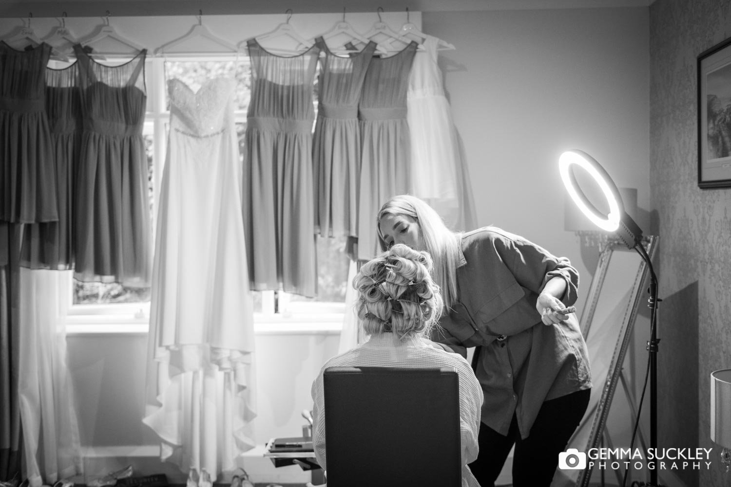 bride getting make up done with wedding dress hung in front of her