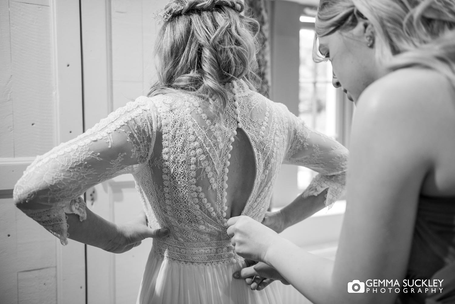 a bridesmaid heloing the bride into her dress at the gamekeepers inn