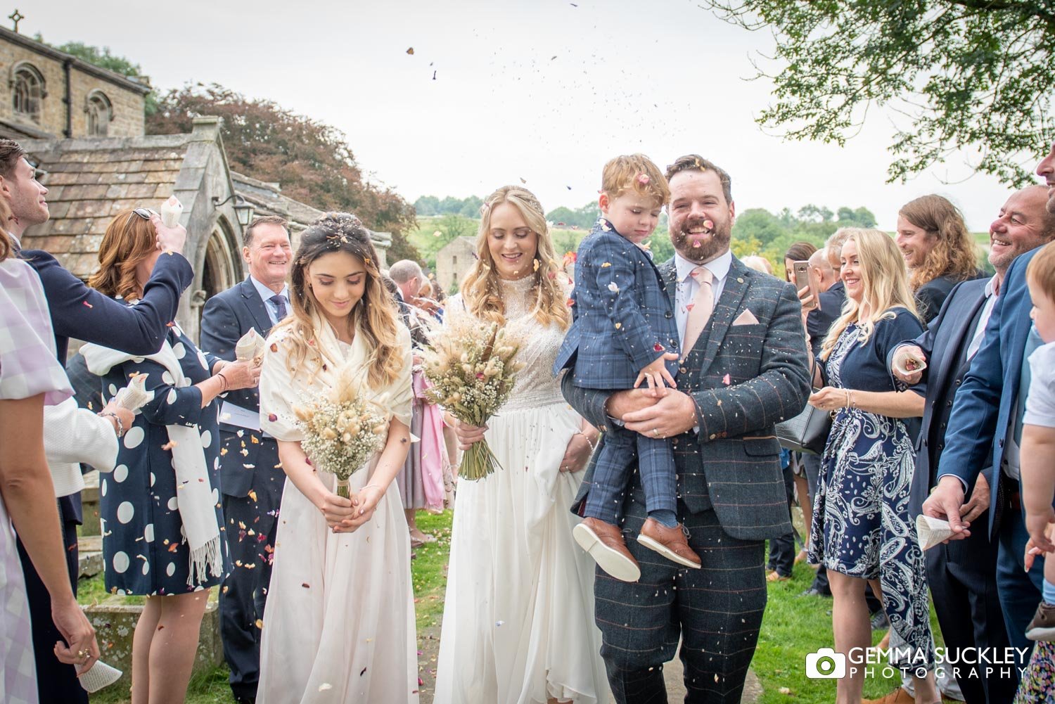 bride and groom with their son and daughter walking as guests throw confetti 