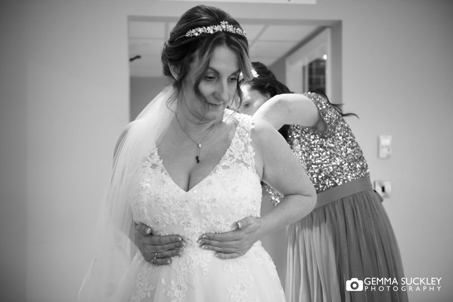 bridesmaid doing up the brides dress