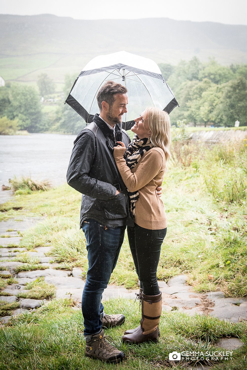 engaged couple holding a umbrella in the rain at burnsall river