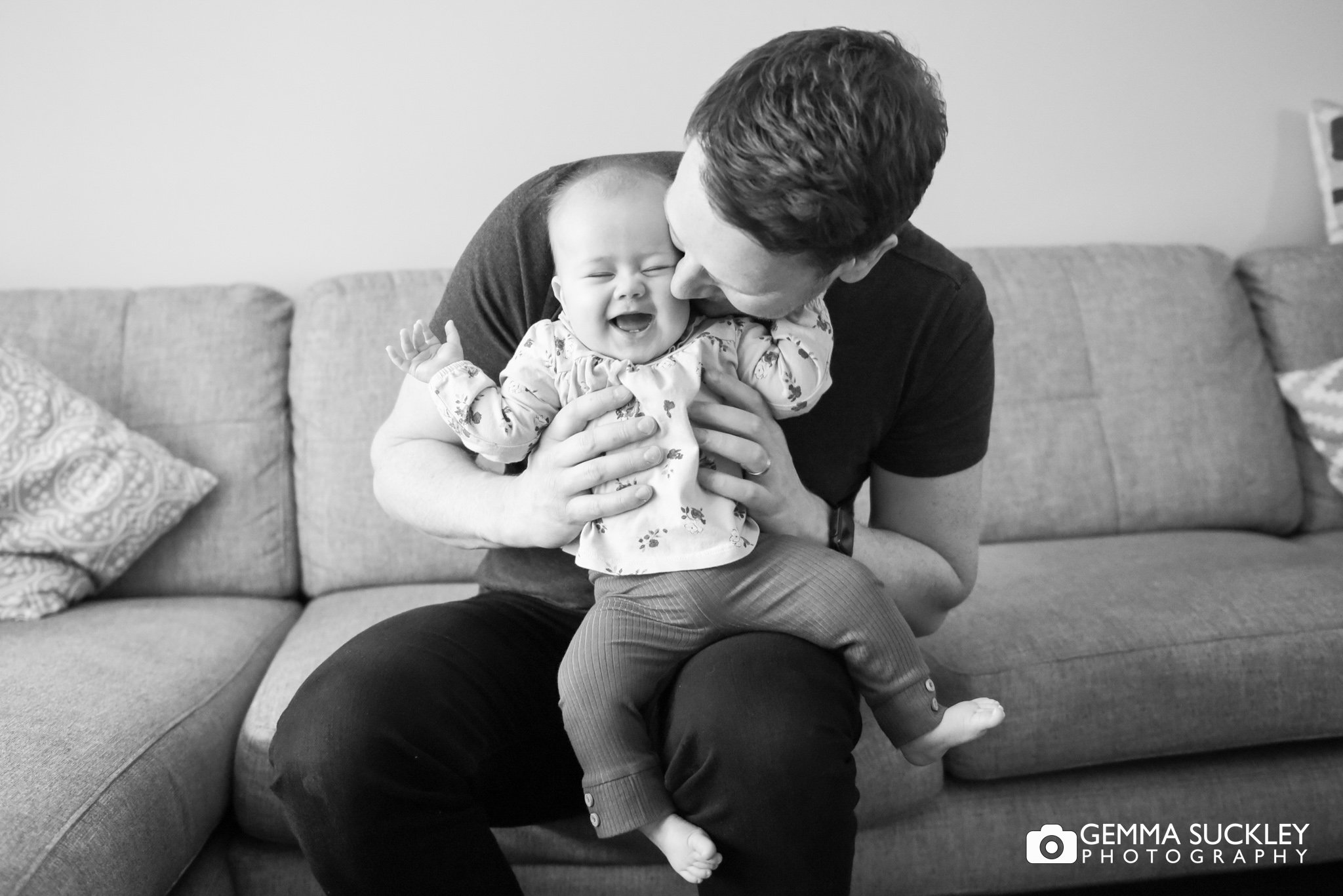 a baby giggling as her dad kisses her cheek