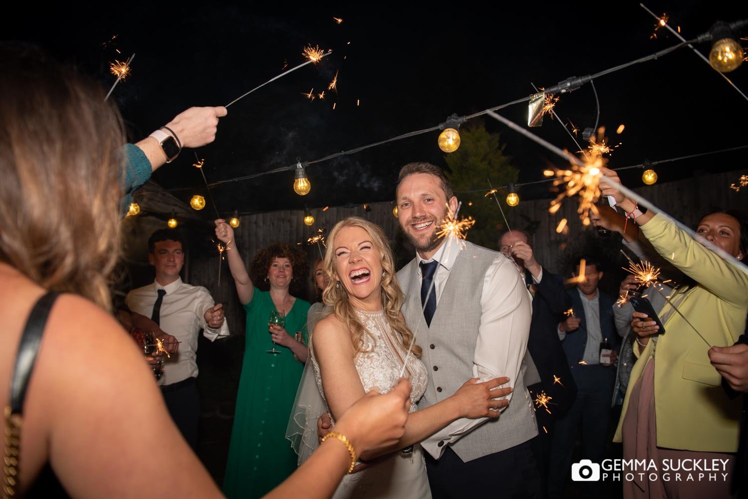 bride and groom laughing as wedding guests hold sparklers around them
