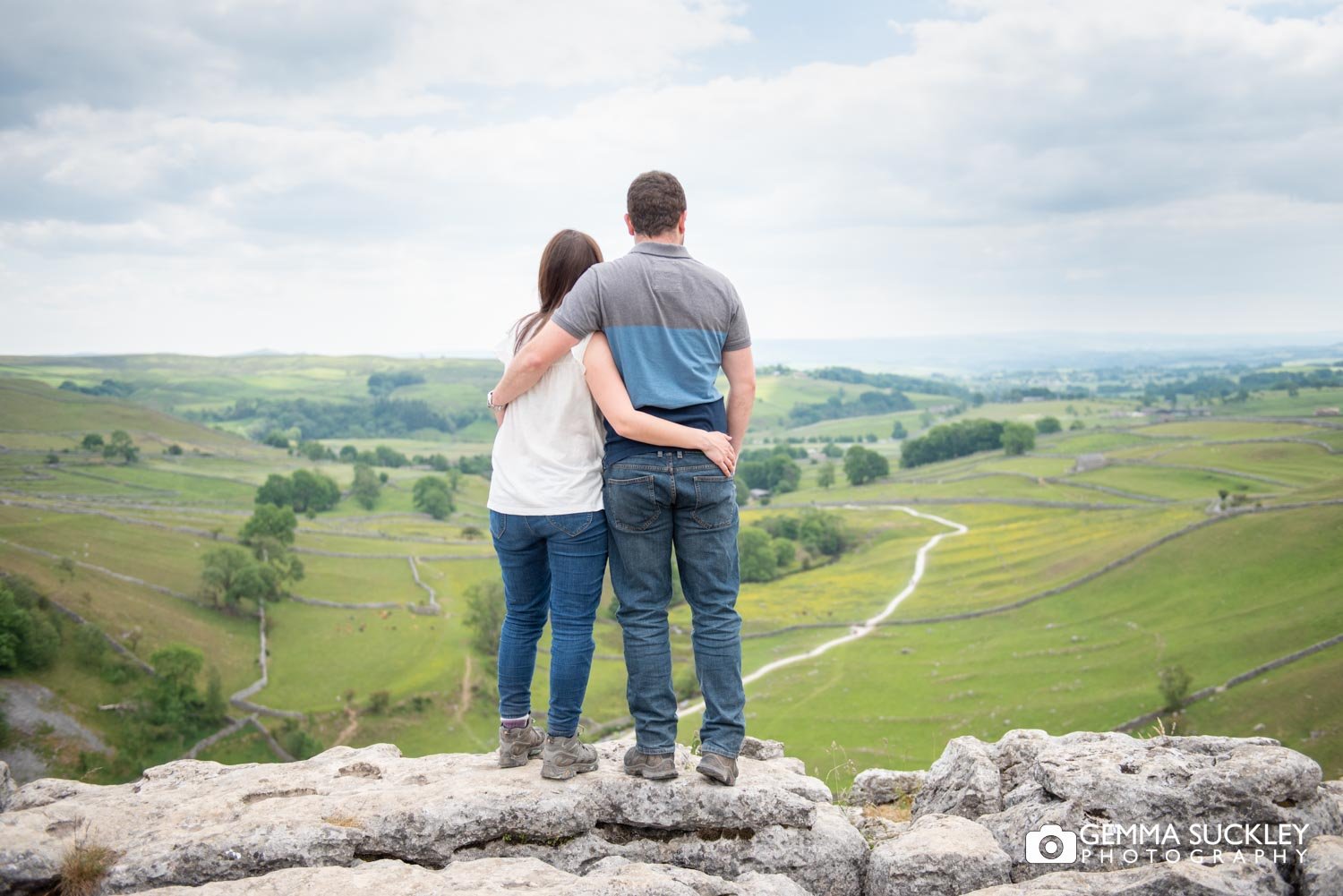 engaged couple arm in arm looing at the view from malham cove