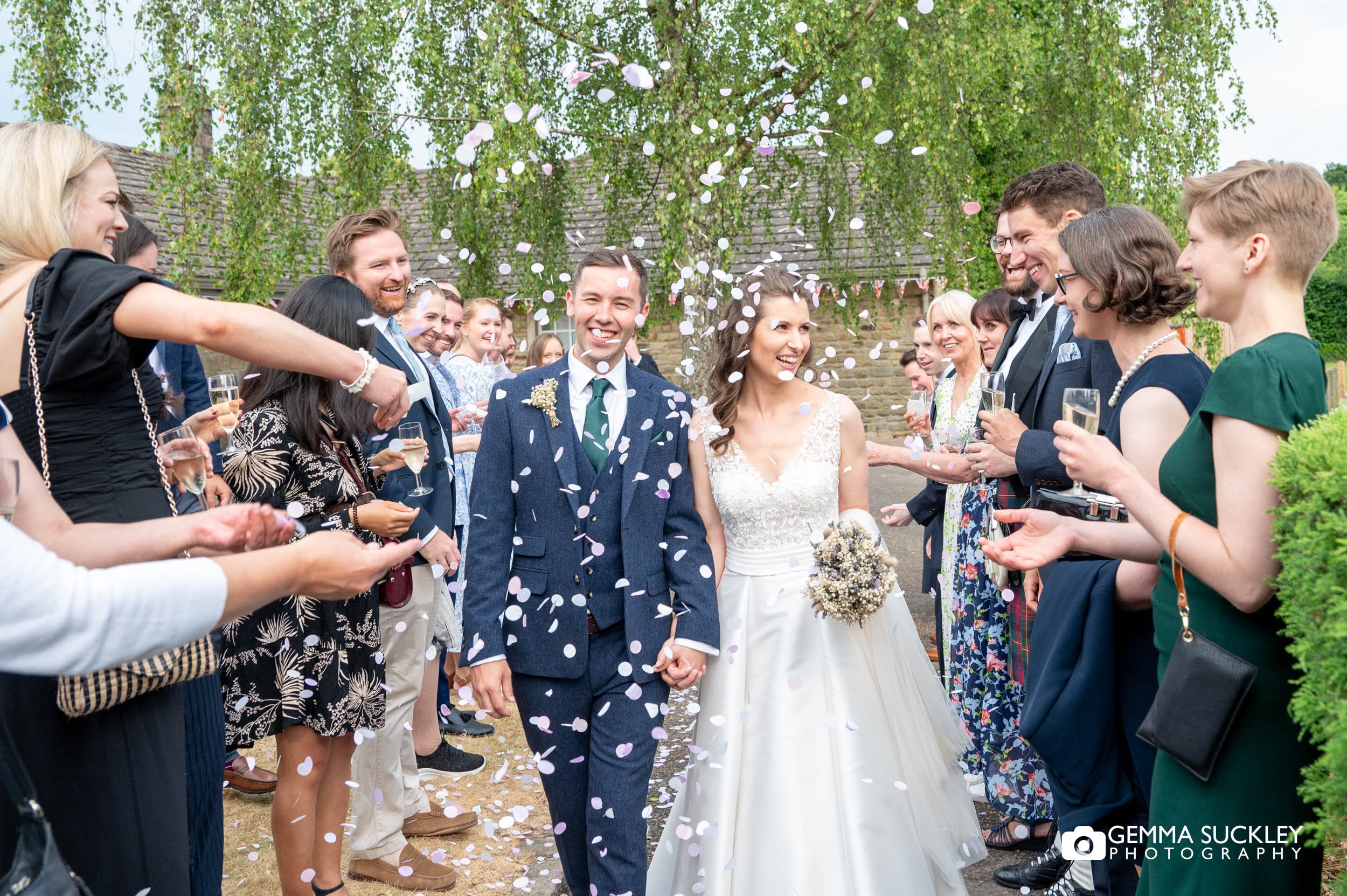 bride and groom walking as guest throw confetti at bolton abbey village hall