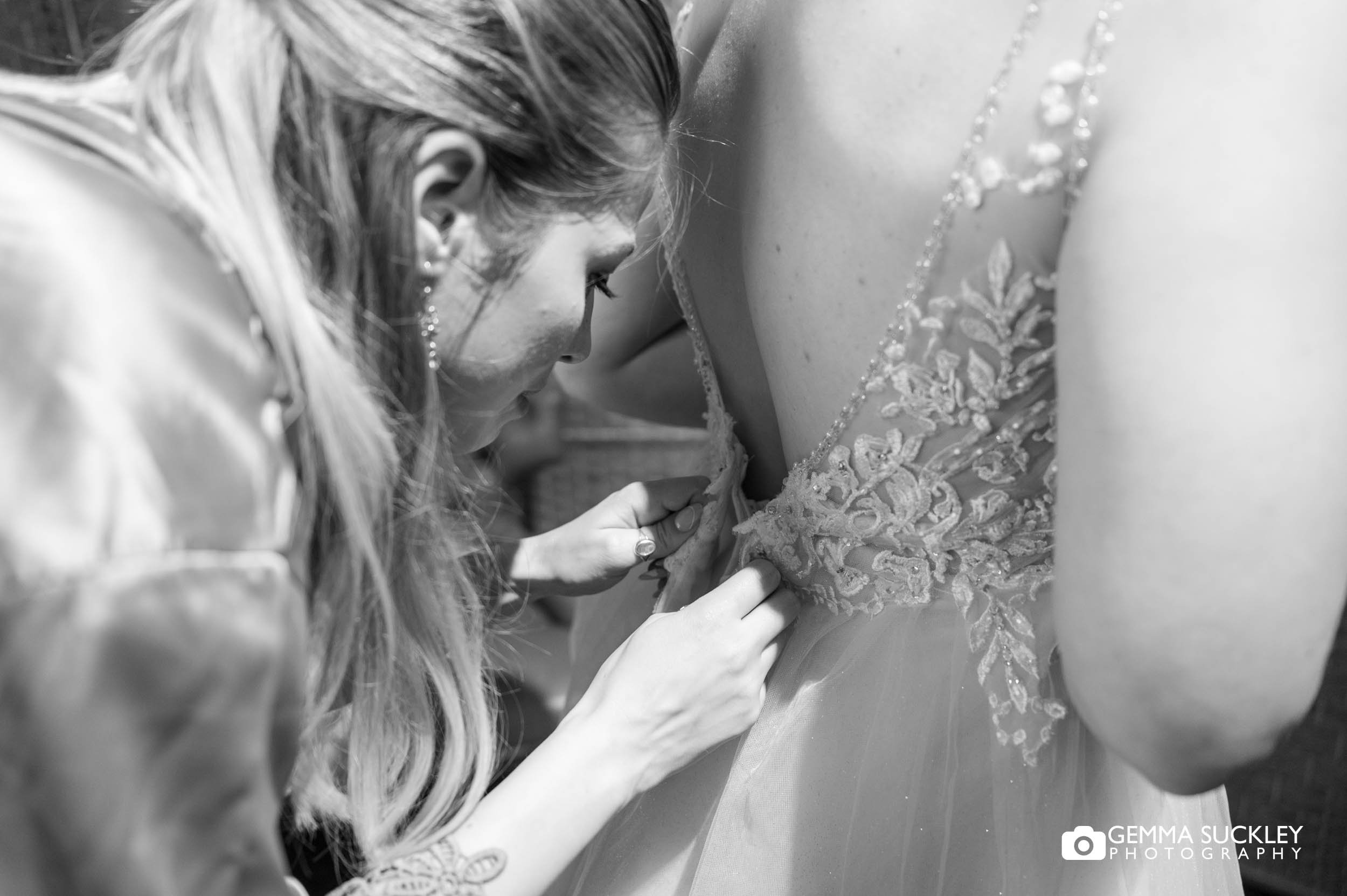 bridesmaid helping the bride into her dress