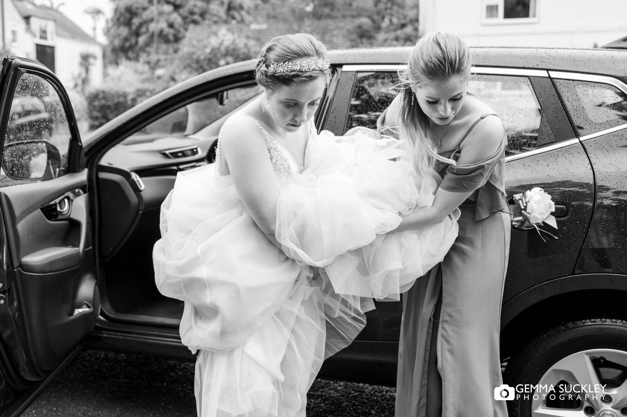 bridesmaid helping the bride out the car with her dress 