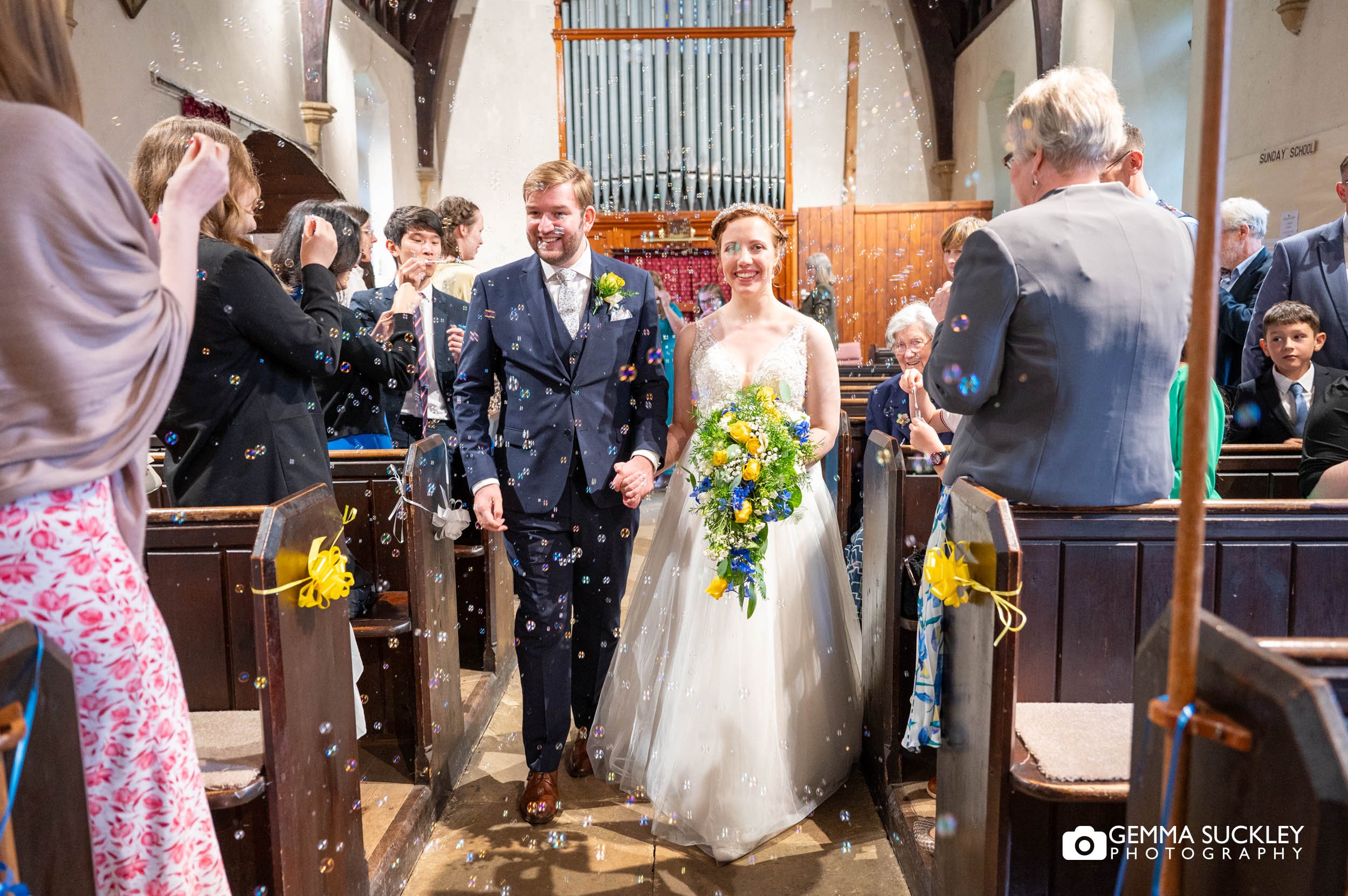 bride and groom exit the church as guests blow bubbles 