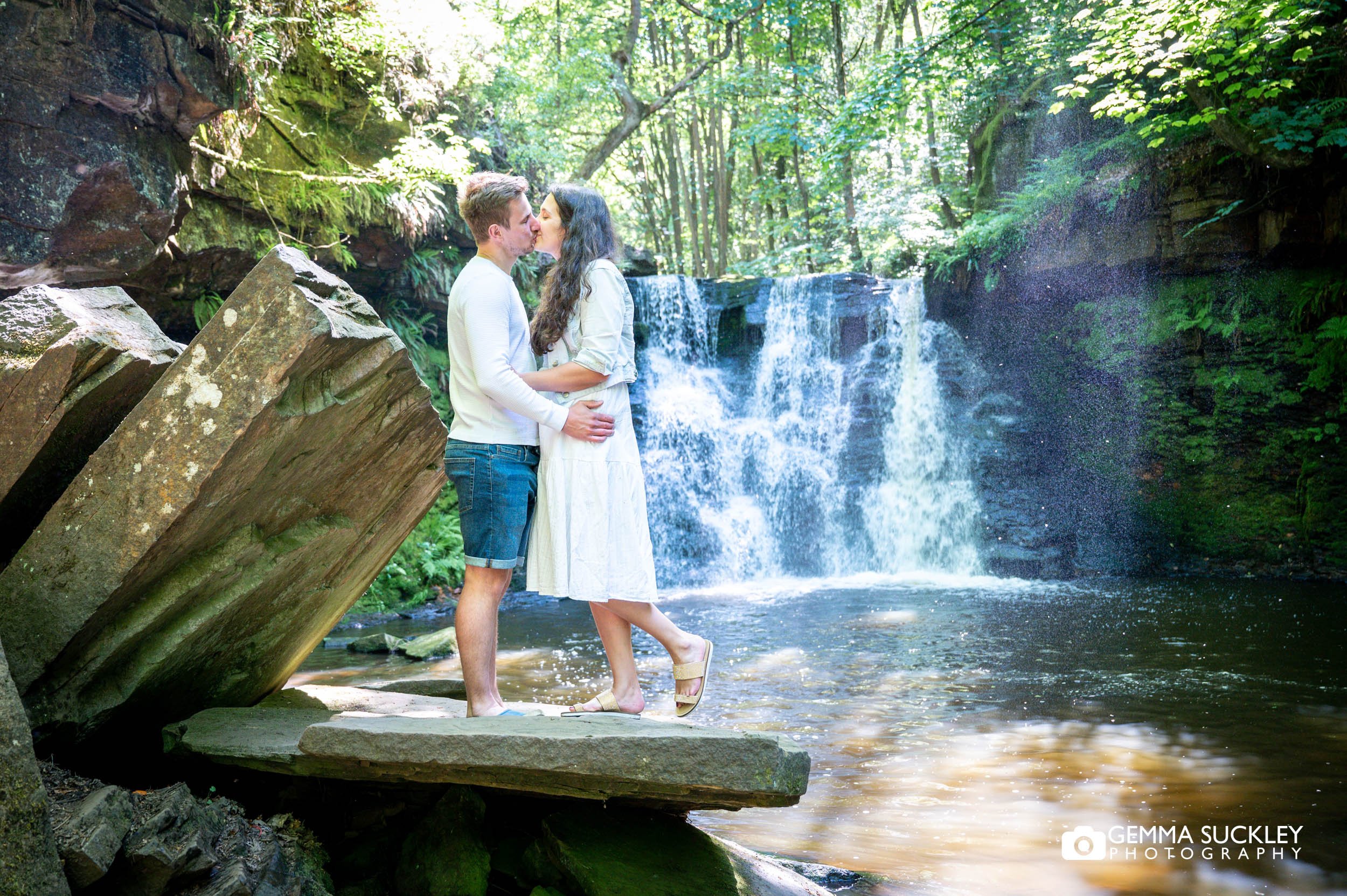 an engaged couple kiss in front of a waterfall