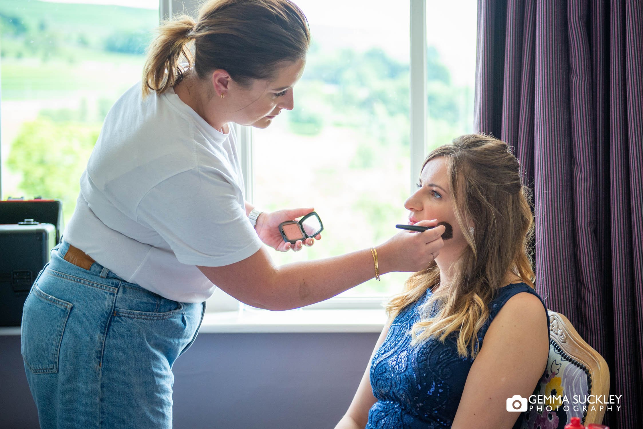 makeup artist applying make up to the bridesmaid