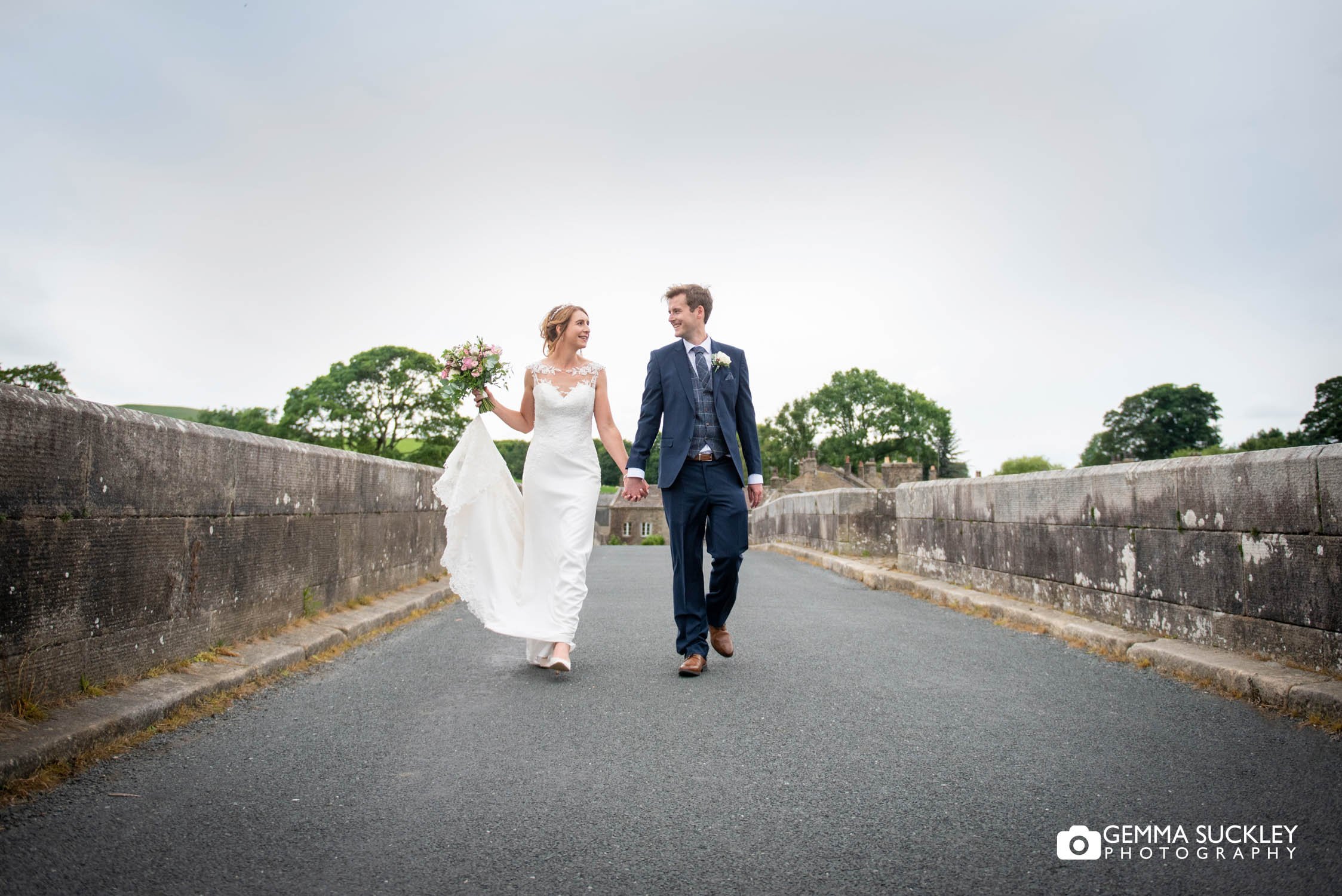newlyweds walking on burnsall bridge