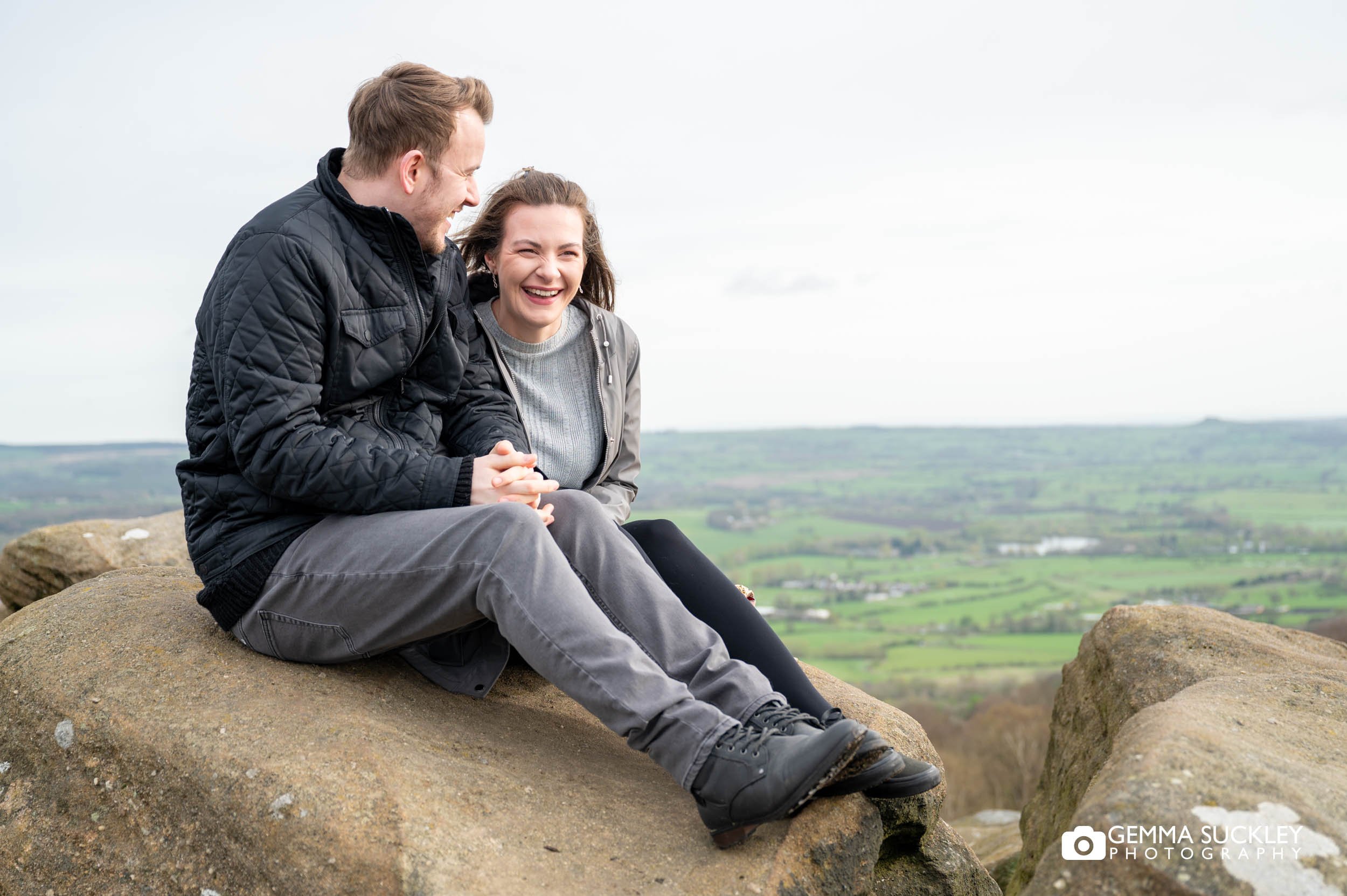 engaged couple sitting on a rock at surprise view at otley chevin