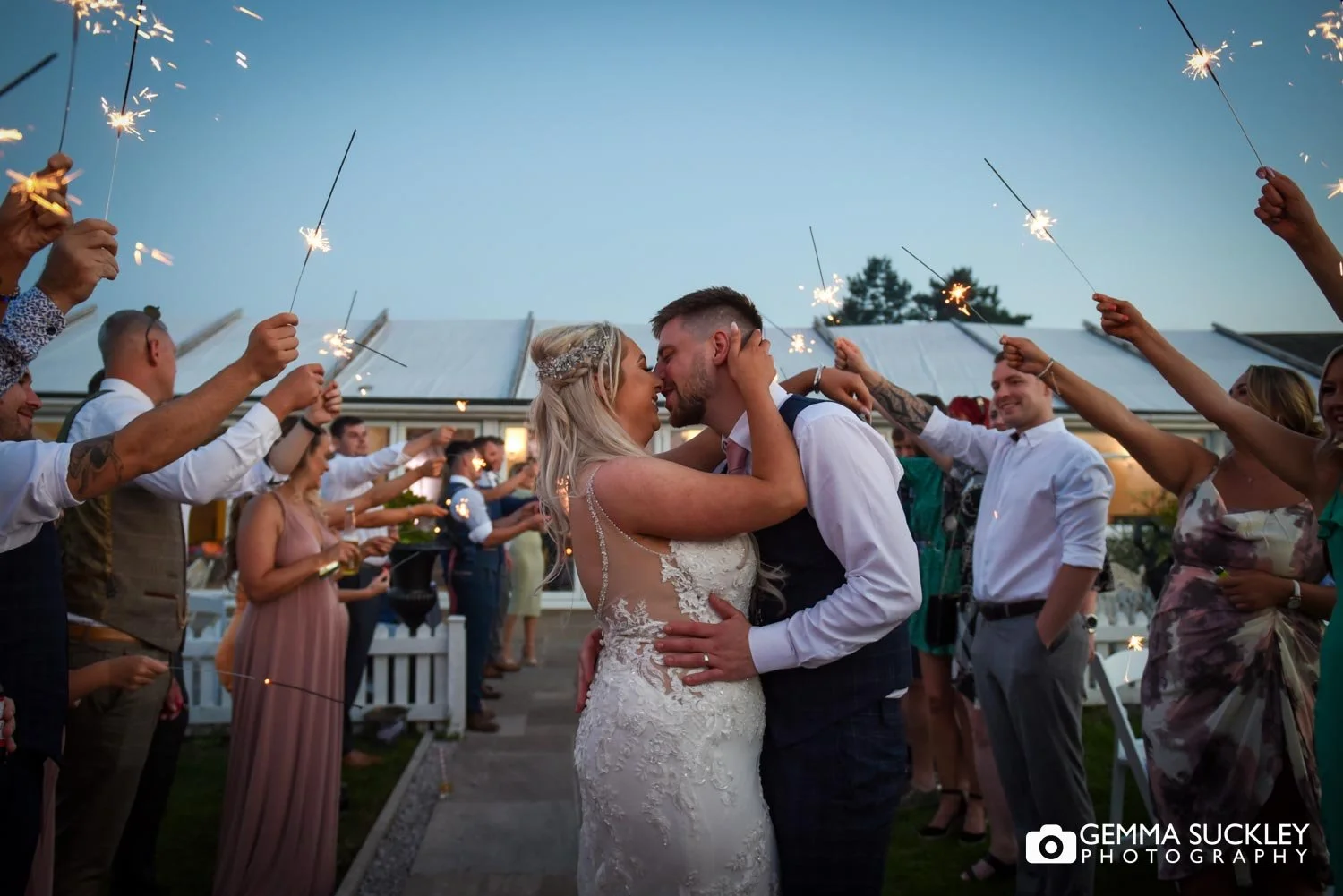 wedding guests holding up sparklers around newly-weds