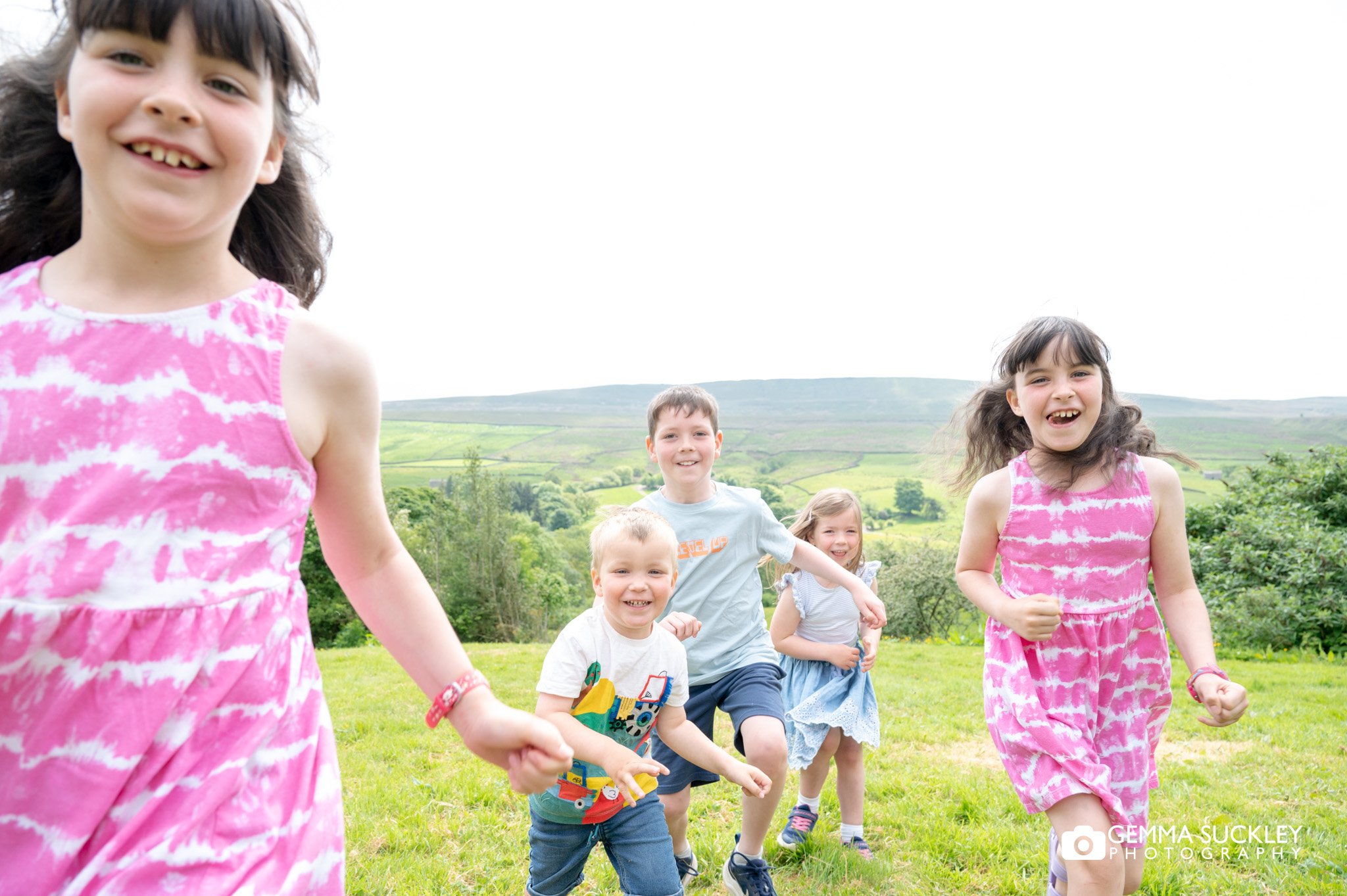 children run towards the camera with a scenic yorkshire dales behindbehind