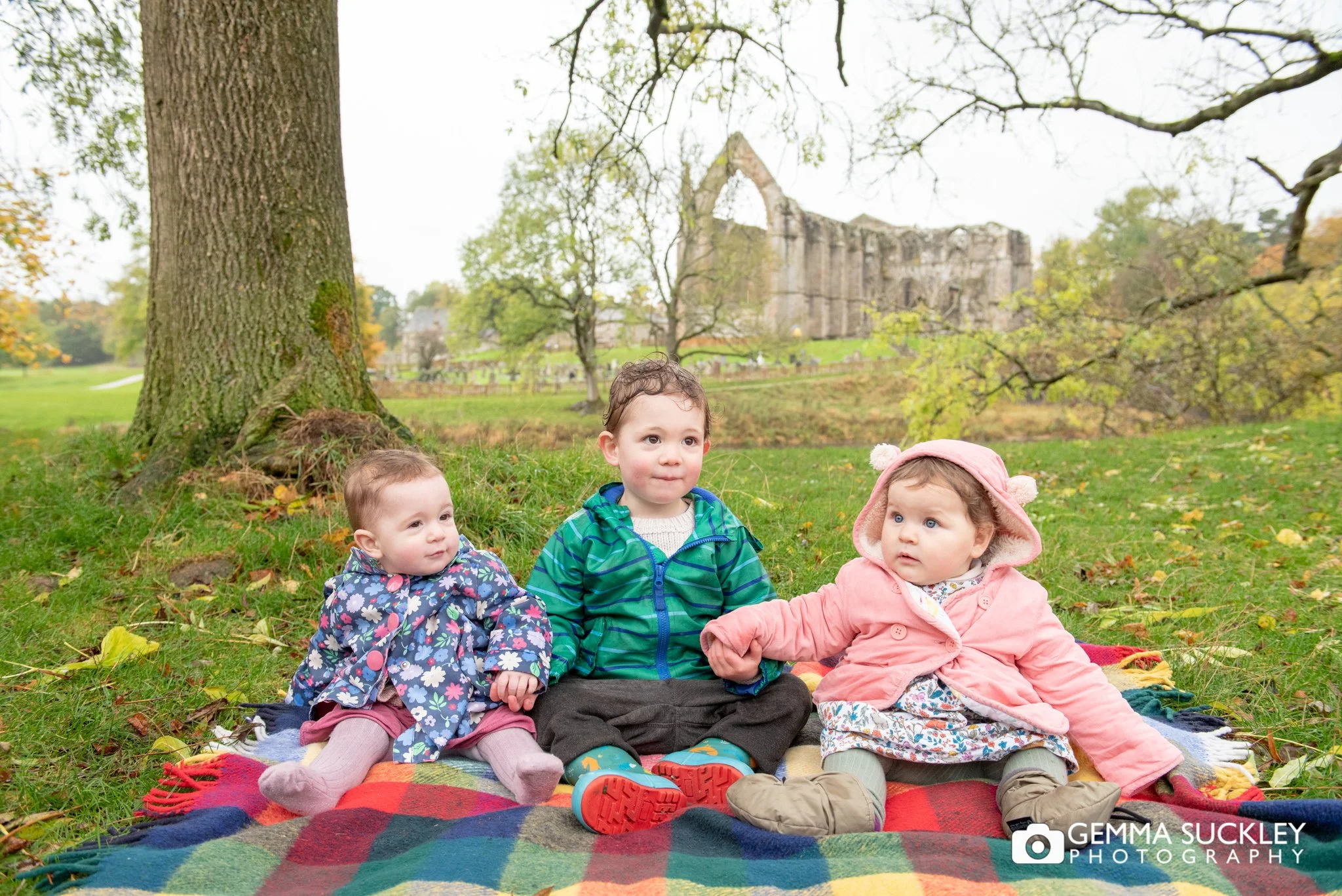 three young children sitting on a blanket at bolton abbey
