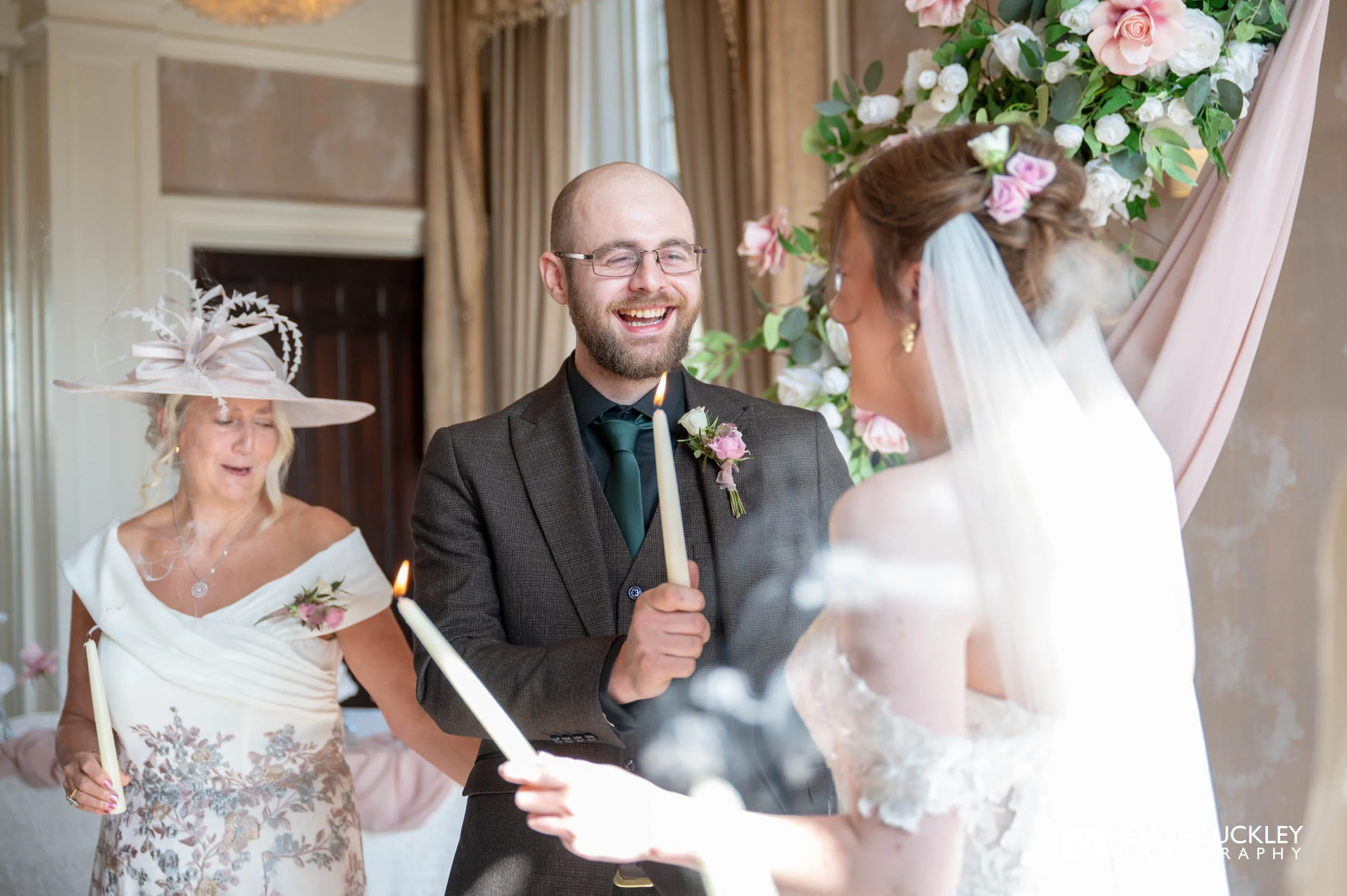 groom laughing as he lights a candle during the ceremony at the falcon manor