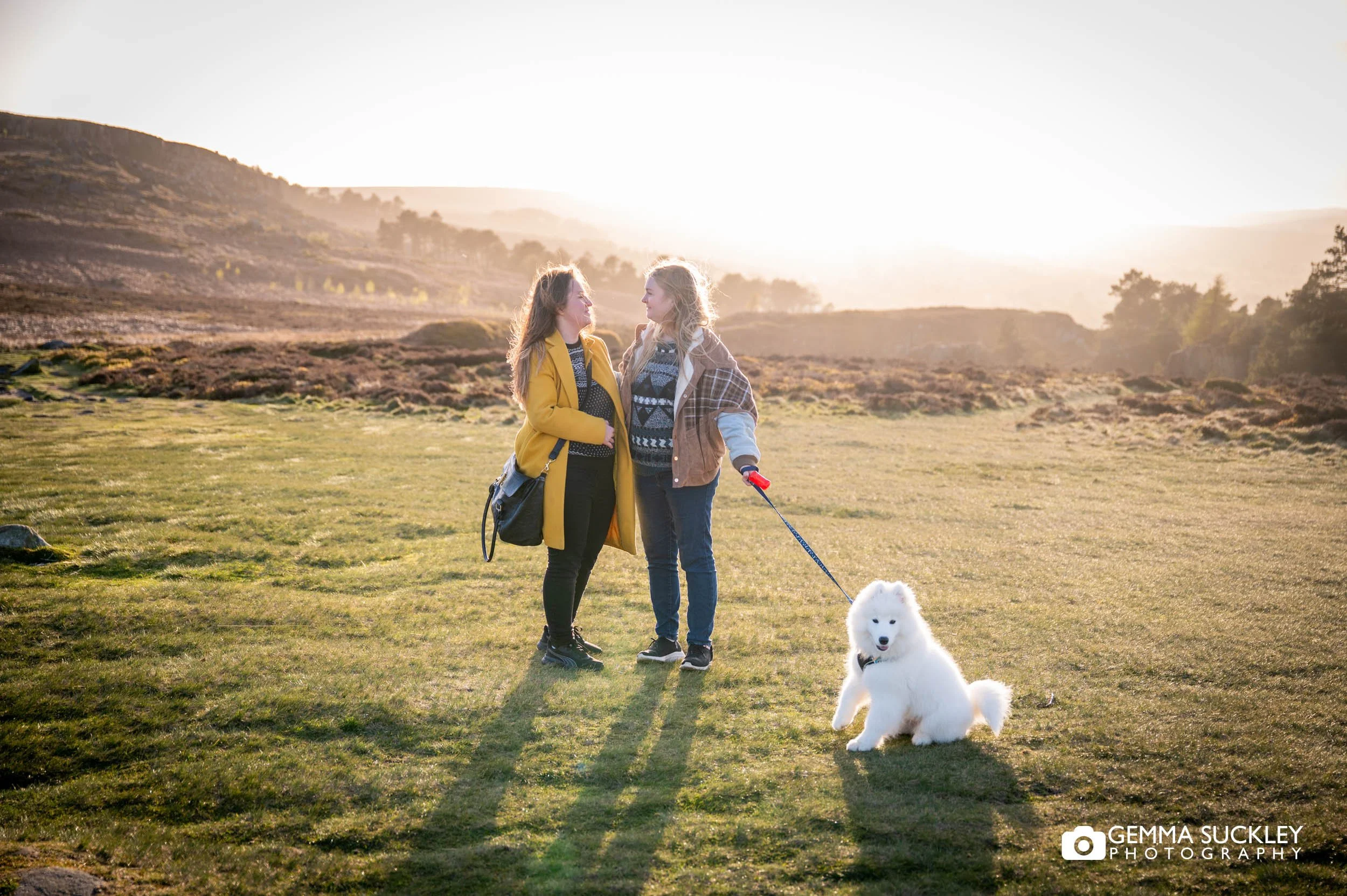 Same-sex couple walking with their puppy on Ilkley Moor during a golden hour pre-wedding photoshoot.