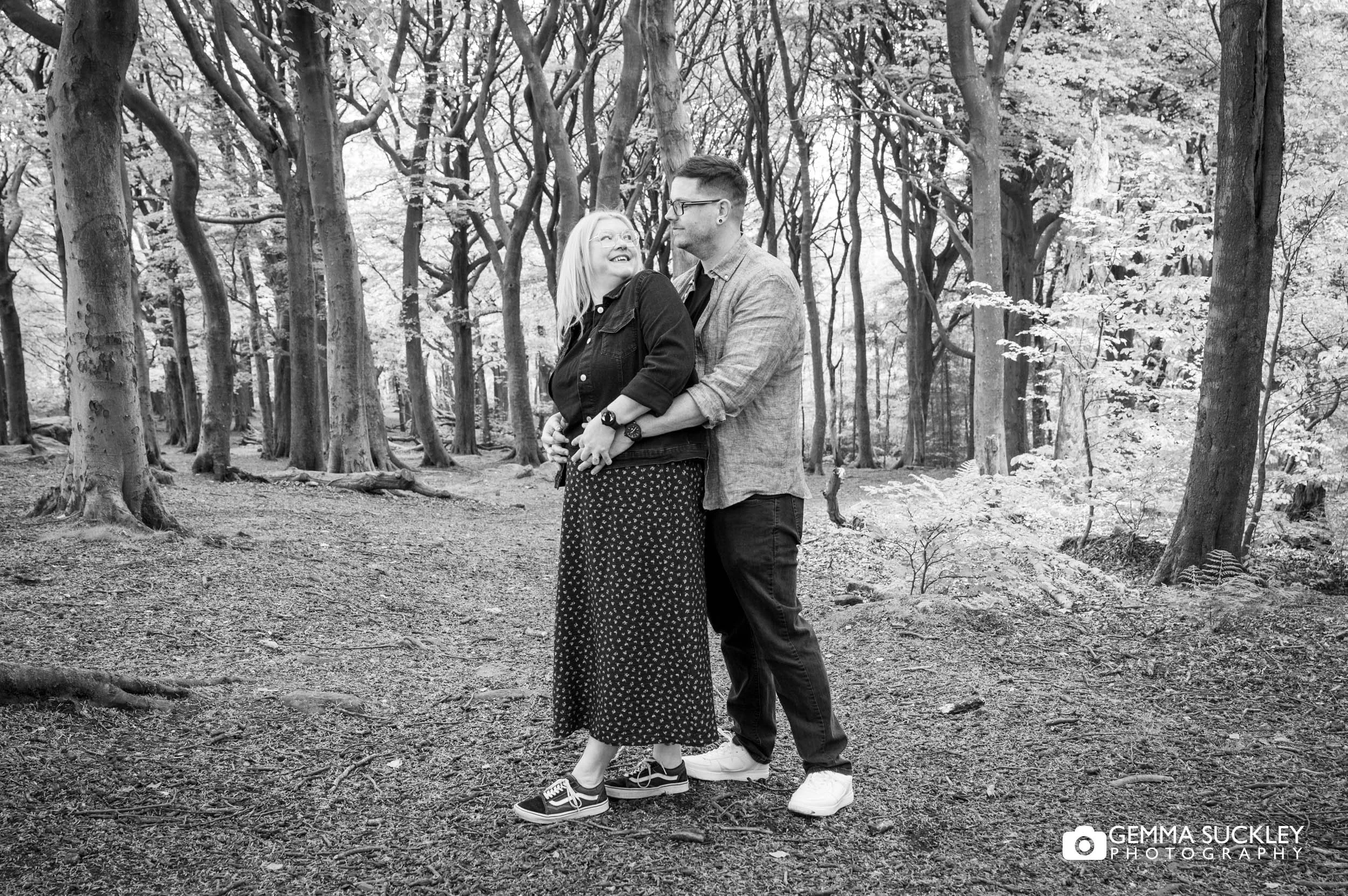 Engaged couple embracing beneath the trees