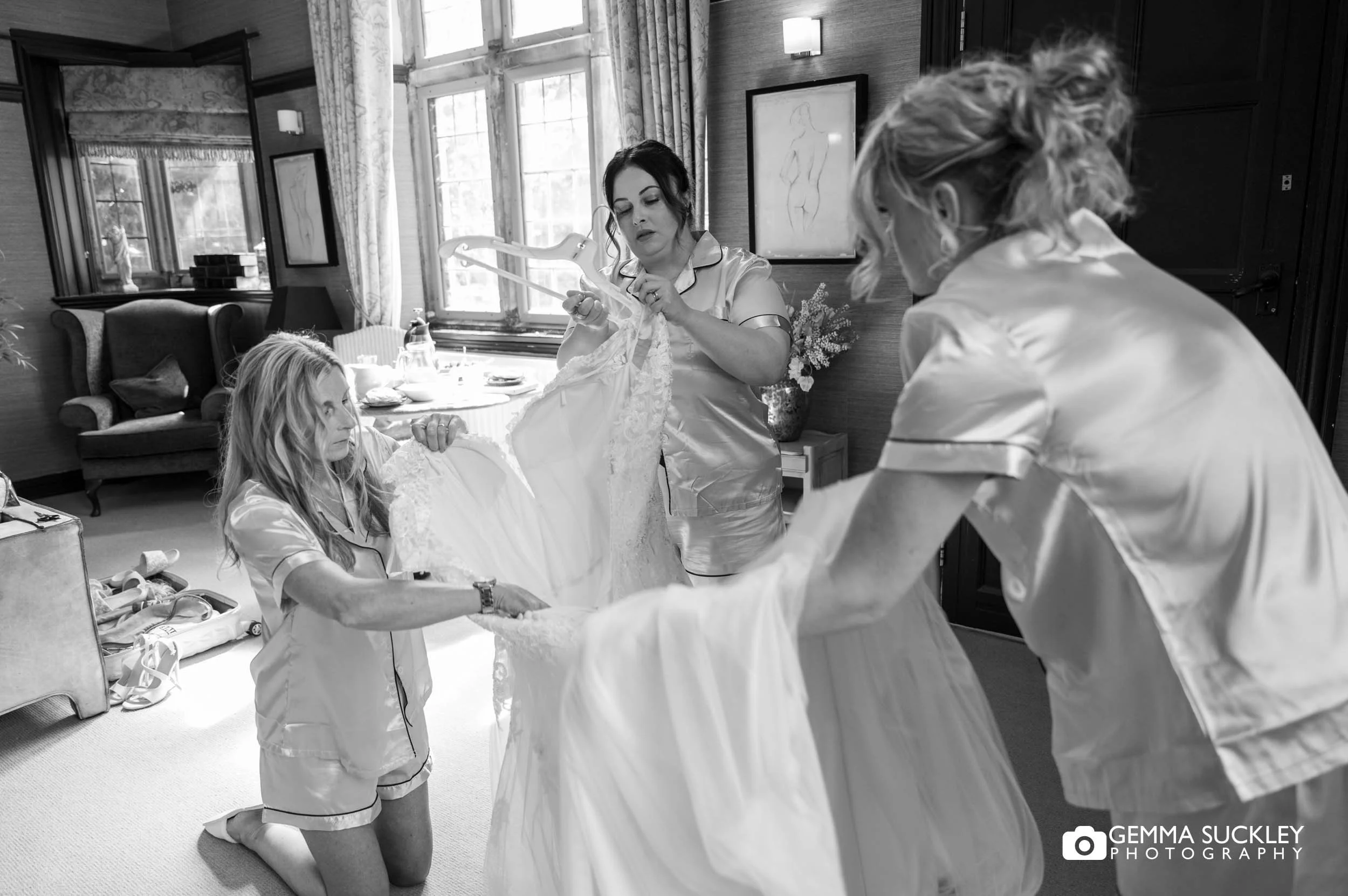 Mother and bridesmaids helping the bride into her wedding dress.