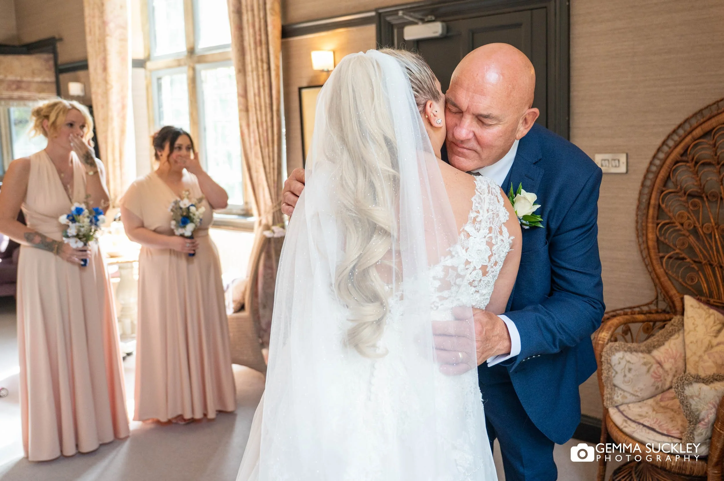 Bride's father kisses her before the ceremony as an emotional bridesmaid wipes away tears