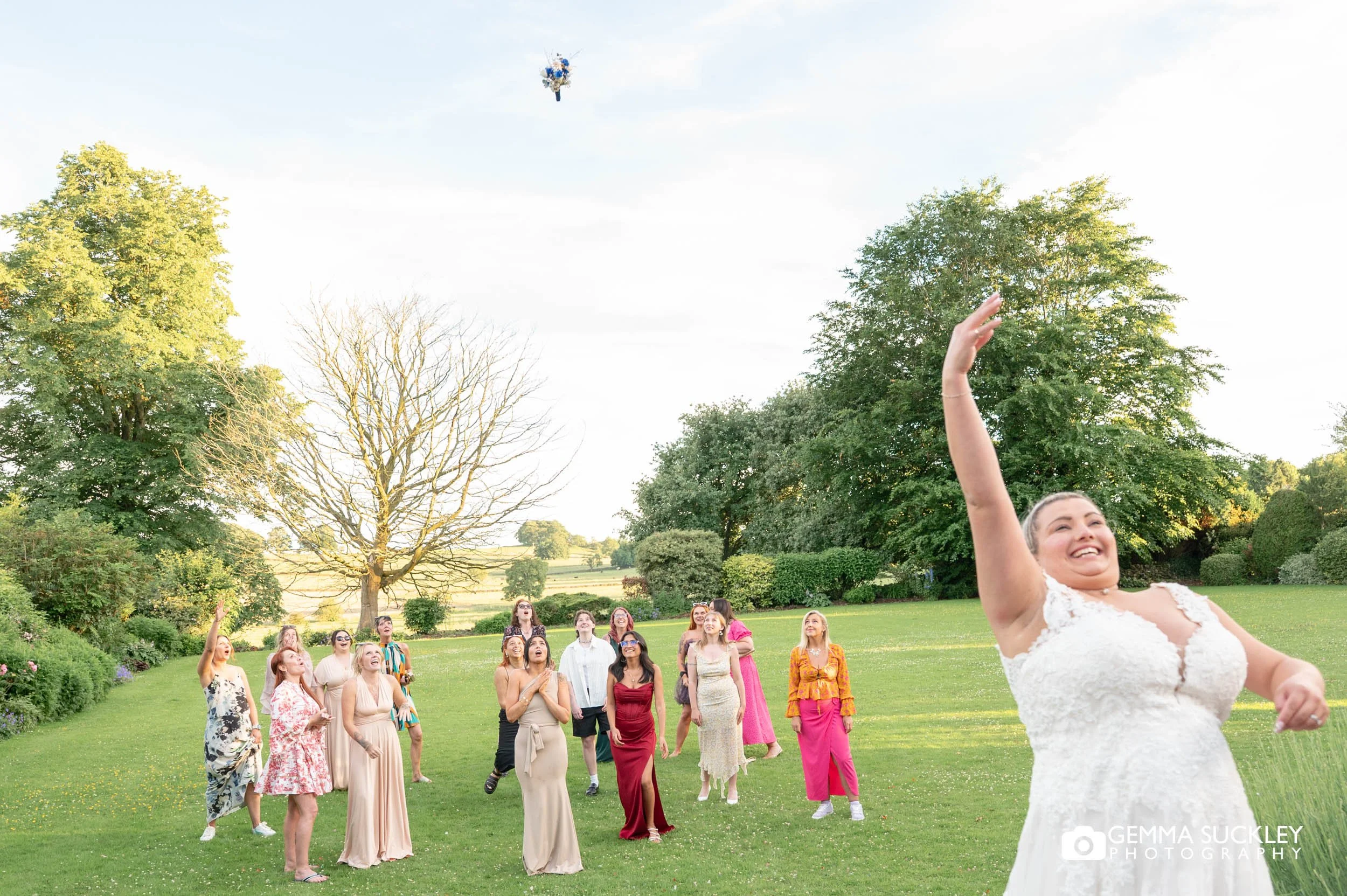 bride throwing her bouquet to guests on the lawn