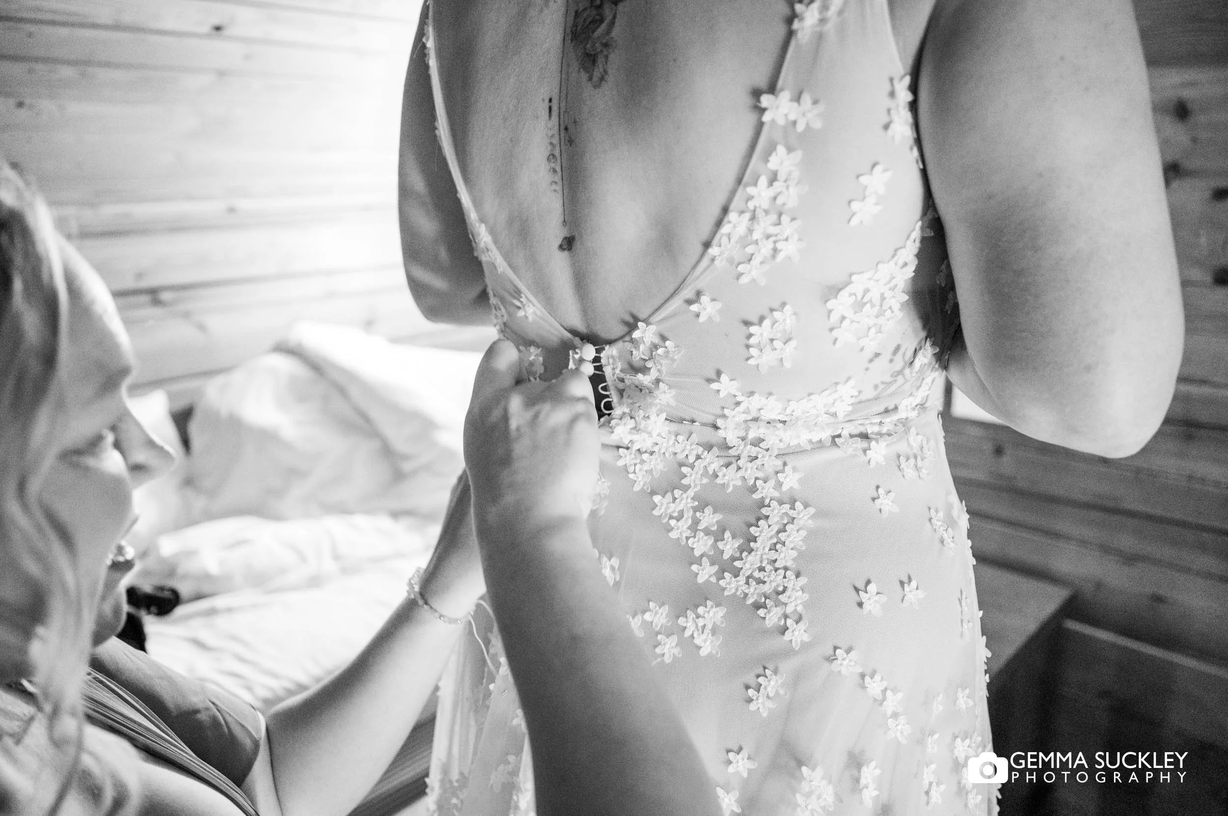 Bride fastening her wedding dress with help from her bridesmaid