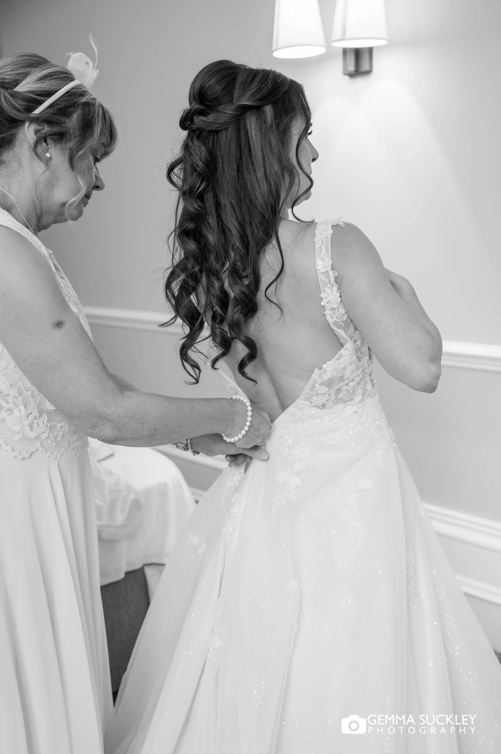 mother of the bride helping her into her dress