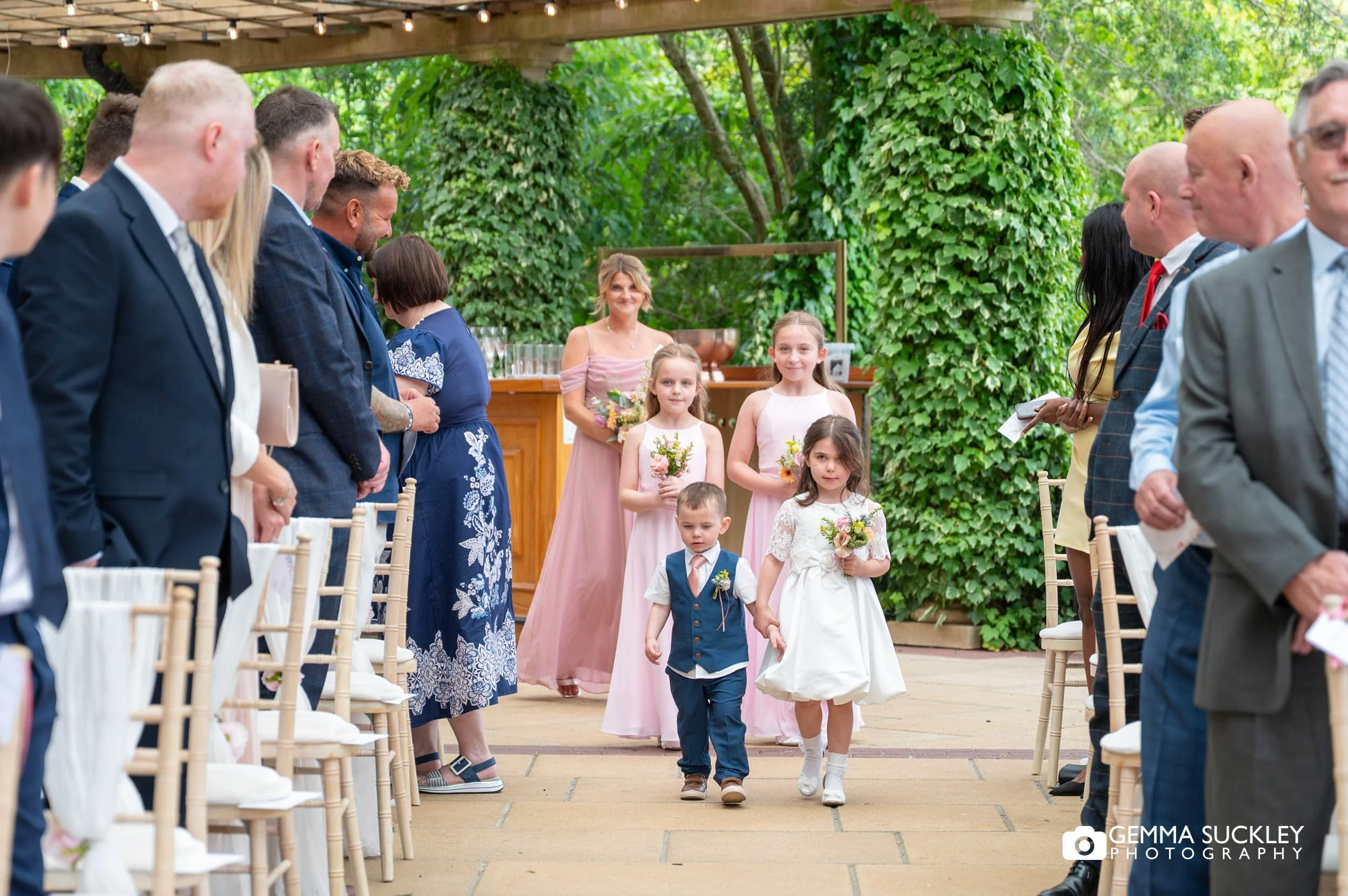 Children walking down the aisle before the bride at outdoor wedding