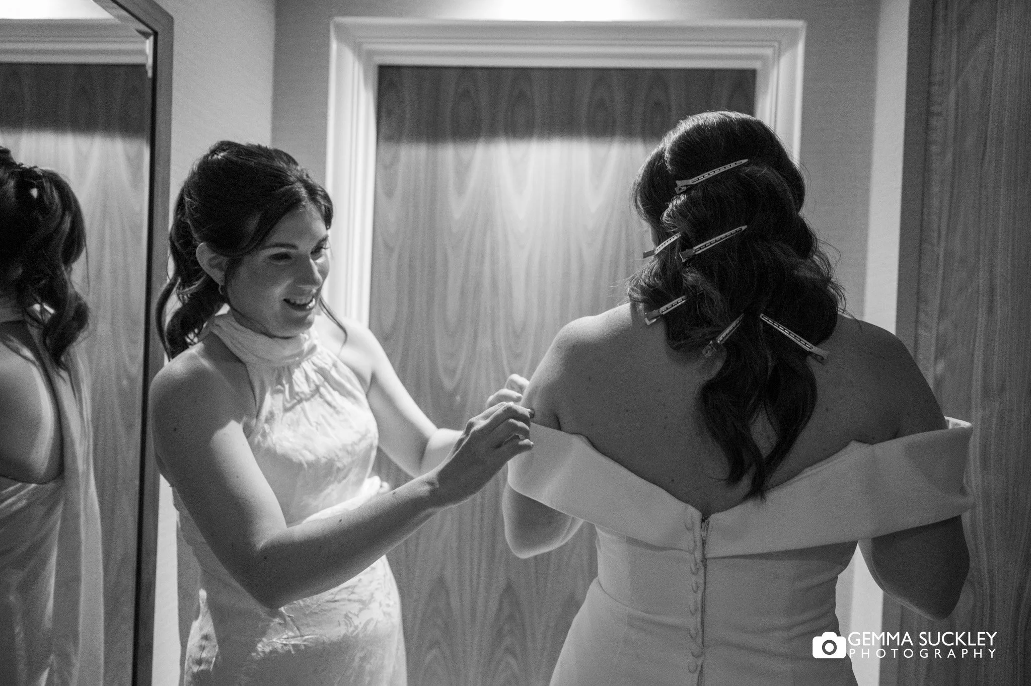 bridesmaid helping the bride into her dress